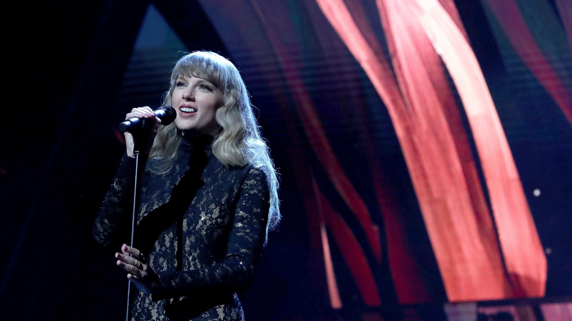 Taylor Swift performs onstage in a black, lace catsuit. 