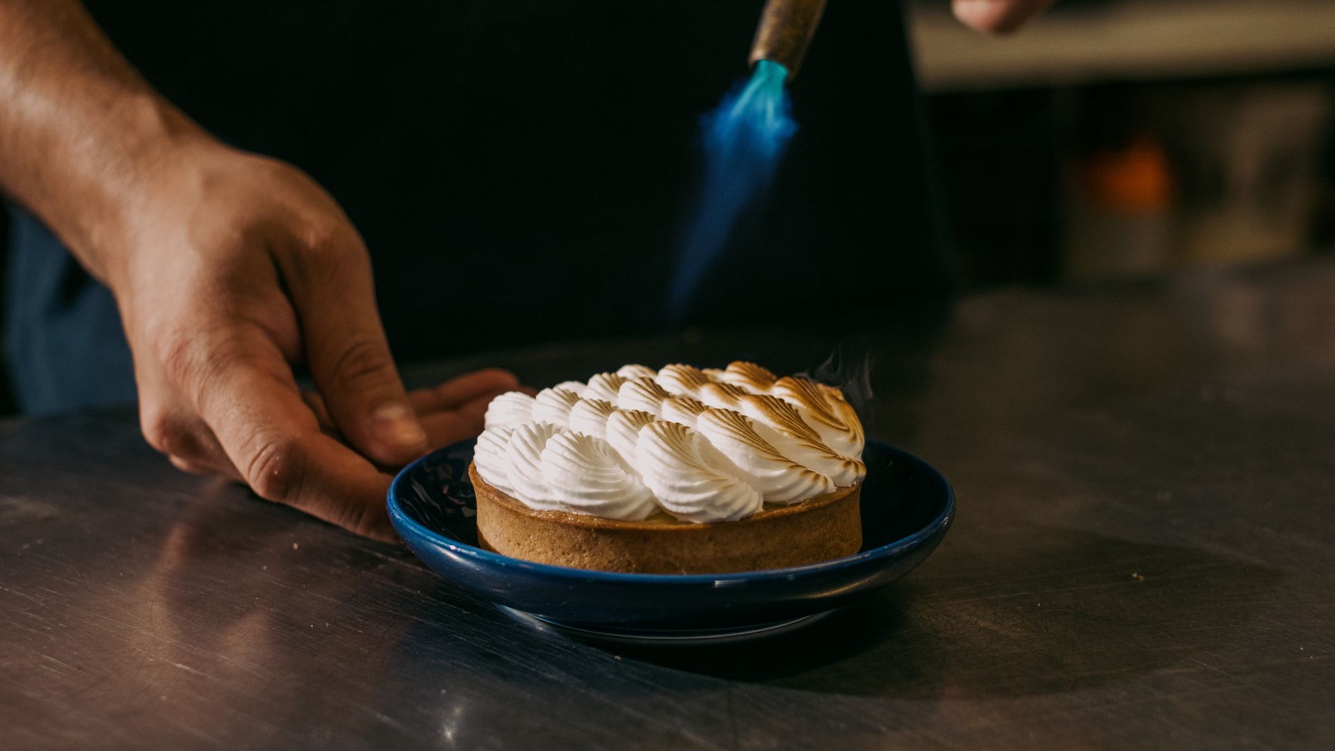 A hand holds a plate with a round, cream-topped pastry on it.
