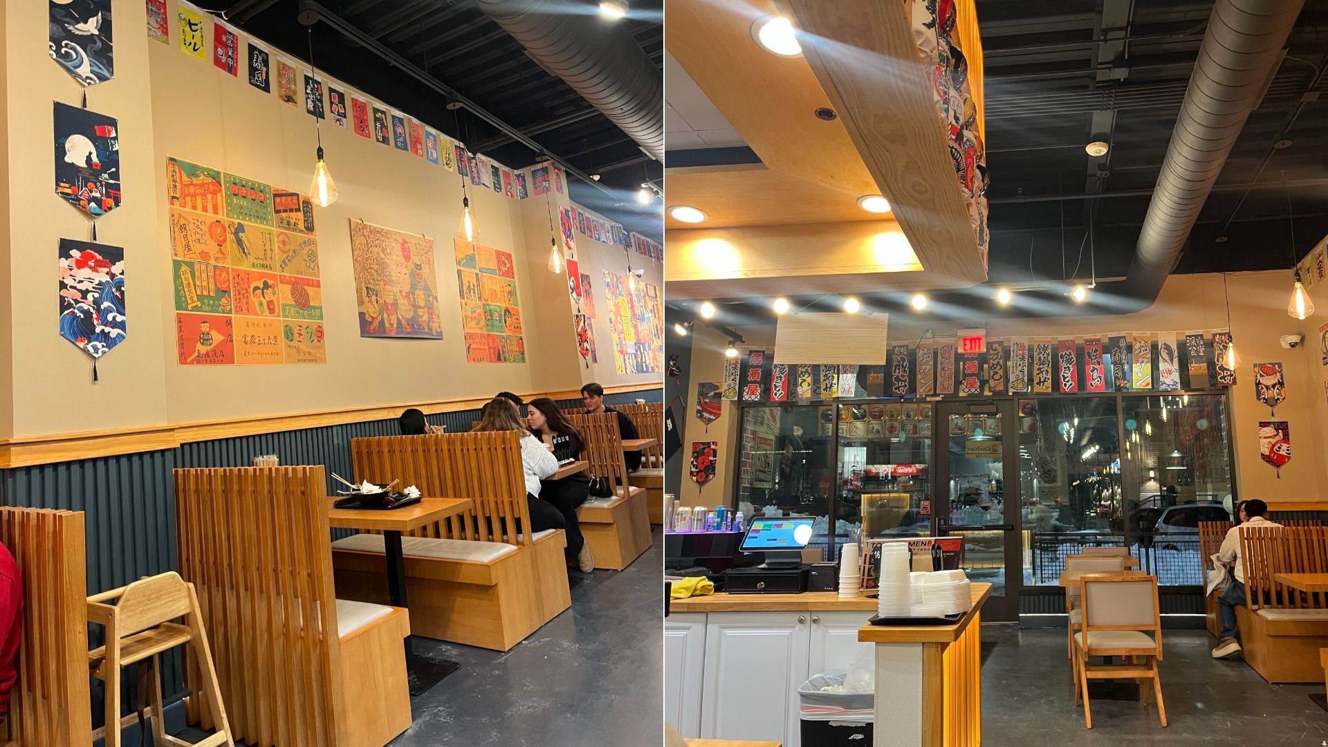 Interior of a Japanese restaurant with wooden booths, colorful Japanese banners and posters on beige walls, hanging light bulbs, and a counter with cups and a register near a glass entrance door.