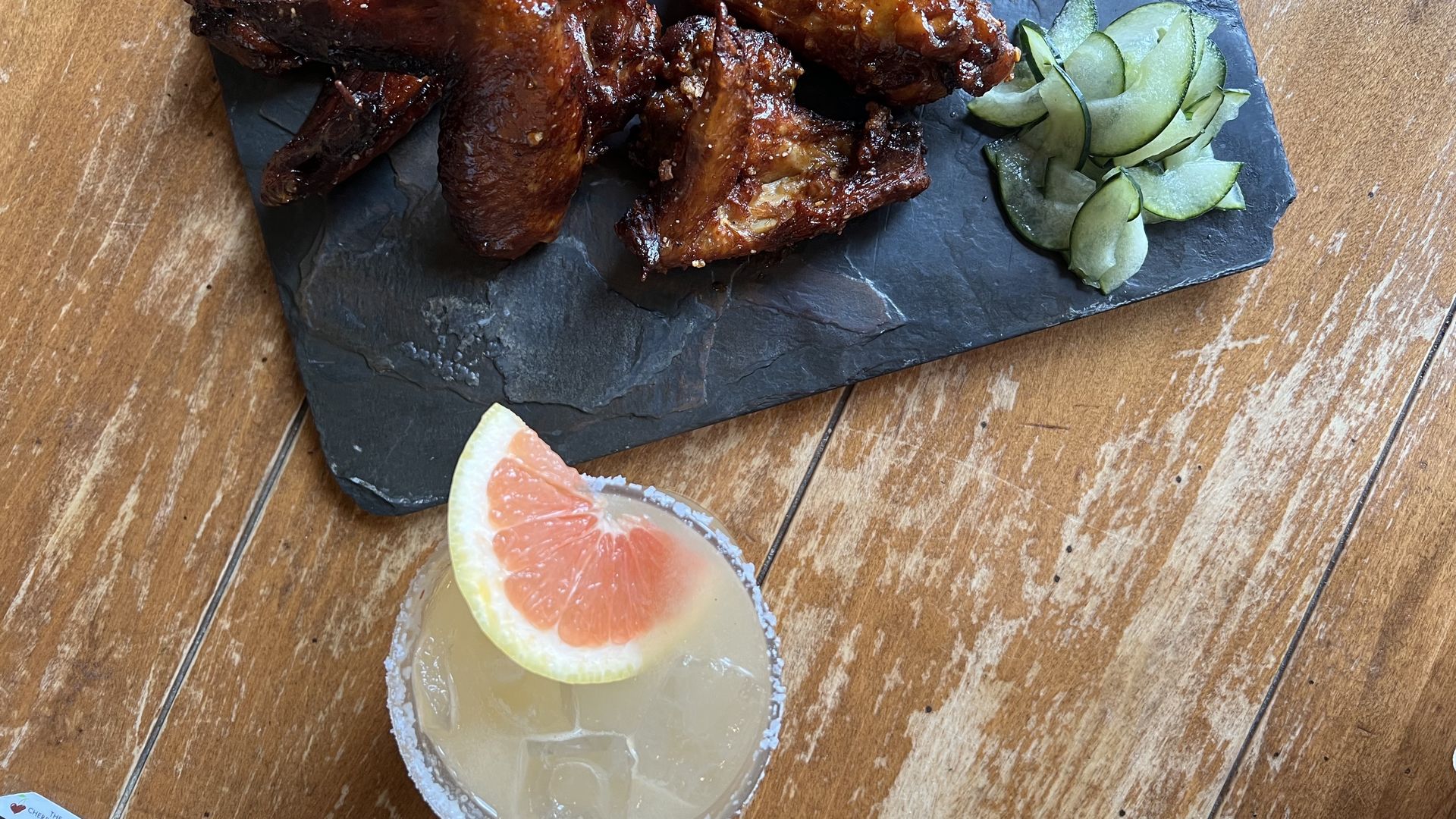 A lightly colored cocktail garnished with grapefruit sitting next to a plate of wings.
