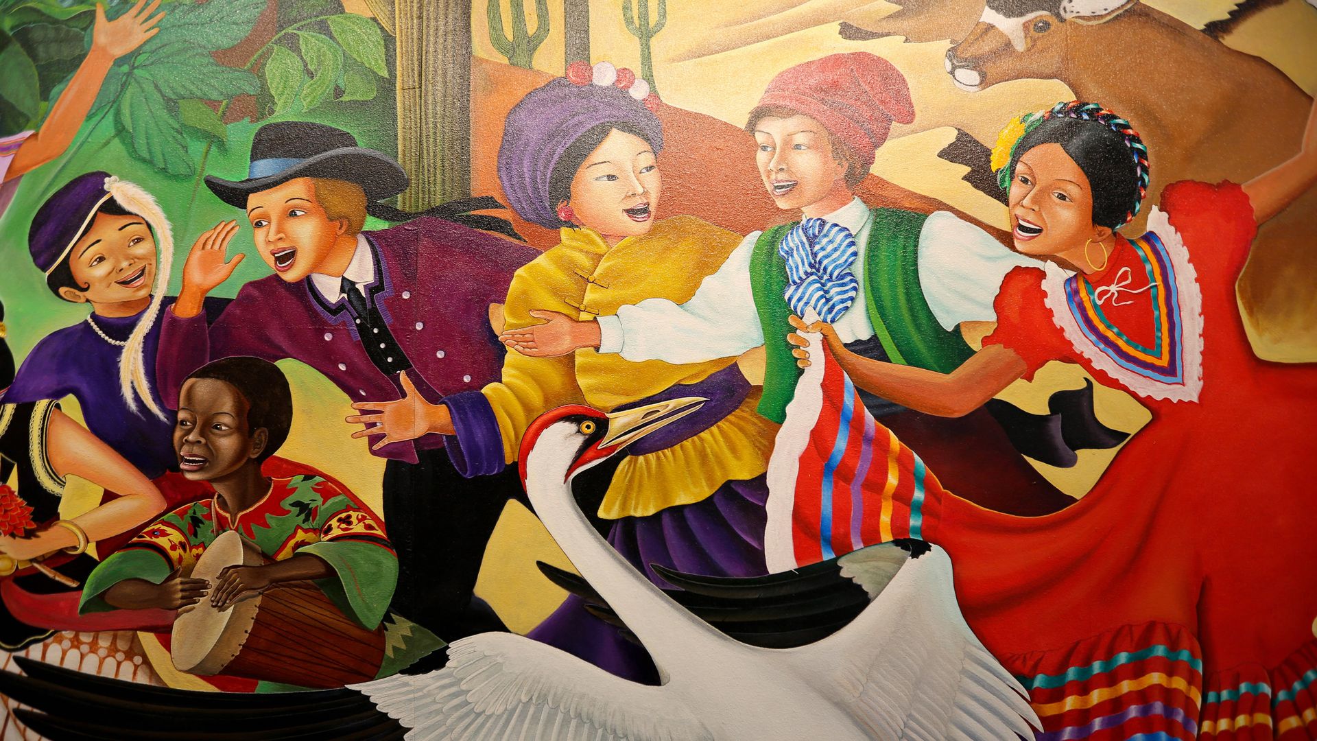 Vibrant mural of joyful people in colorful traditional clothing dancing together, wearing turbans and headwraps, with a white bird in the foreground; bright orange, yellow, and green background.