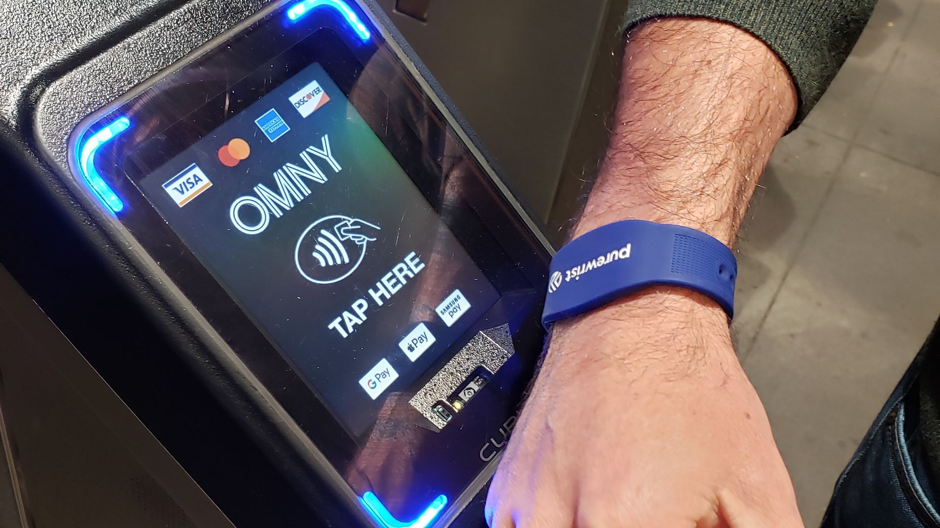 An arm swiping a payment bracelet against a subway payment terminal