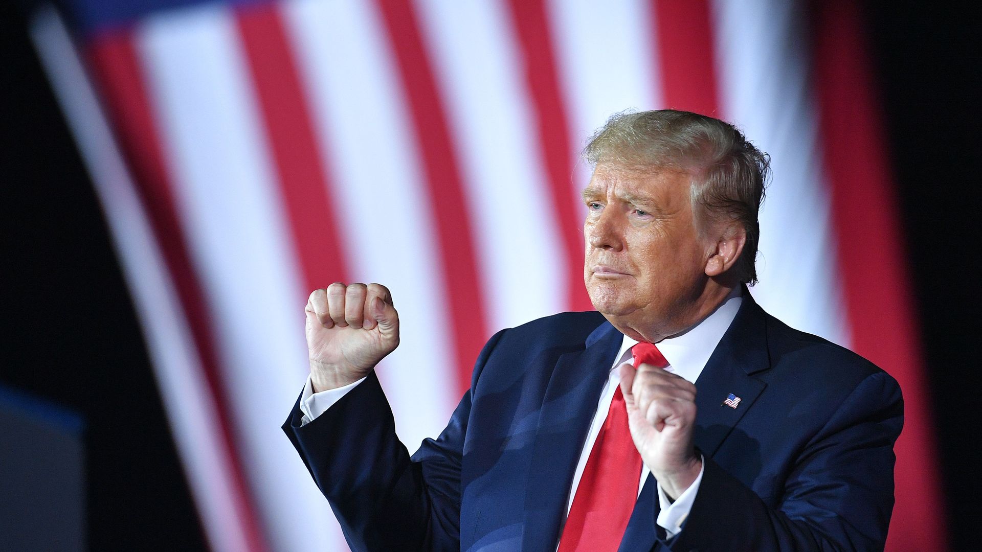 Trump holds his fists in the air in a celebratory gesture while wearing a suit