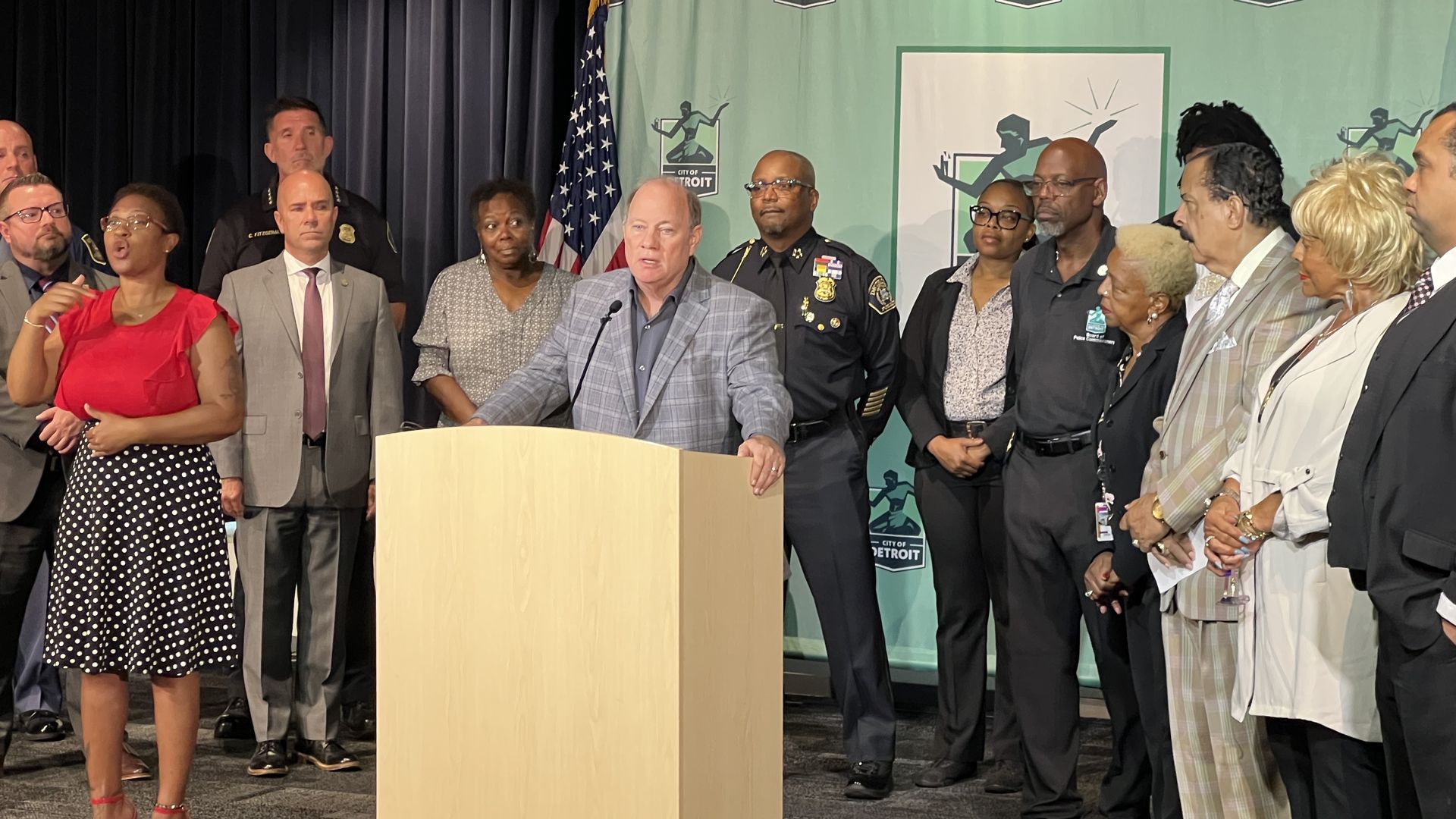 Mayor Mike Duggan stands behind the podium in front of a group of city officials including Detroit police chief James White. 
