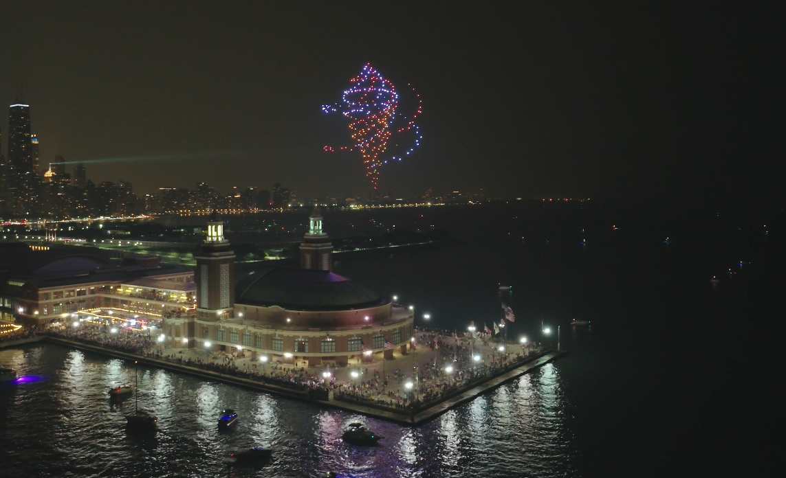 Photo shows drones lighting up and making shapes in the sky above Navy Pier in Chicago.