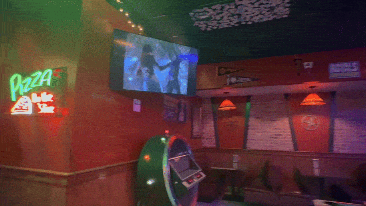 Dimly lit pizza parlor interior with neon green and red "Pizza" sign, vintage jukebox, red walls with sports pennants, and a television mounted showing a game. Booth seating visible.