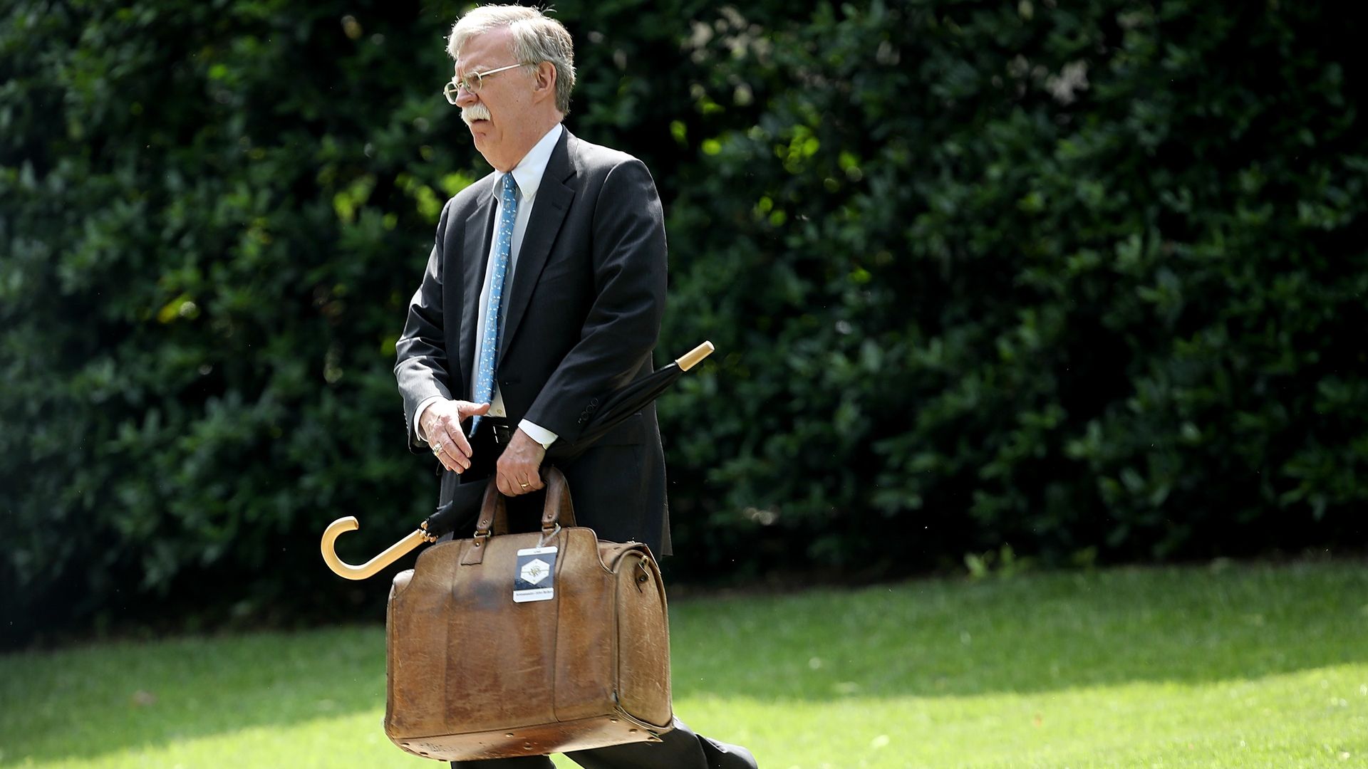 John Bolton carrying luggage and umbrella