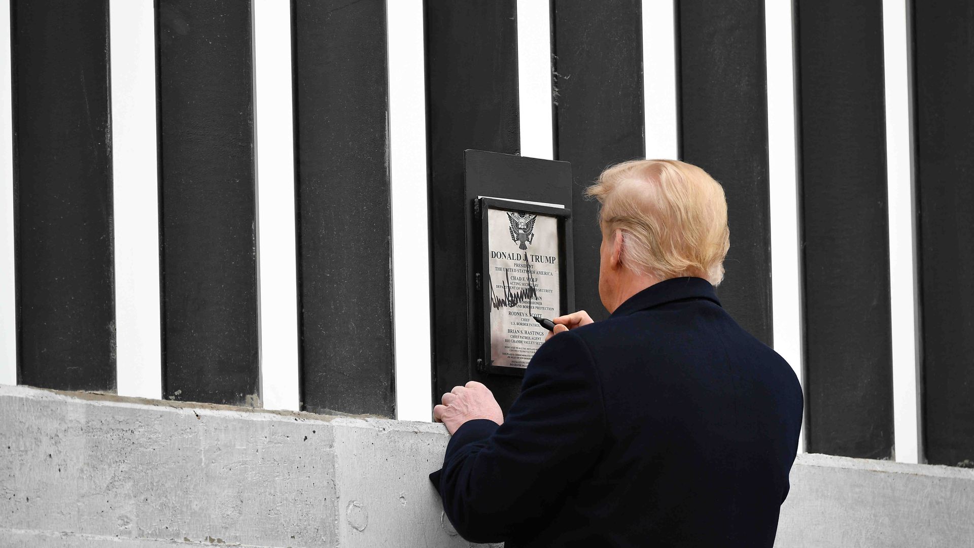 President Trump is seen signing a plaque on the U.S.-Mexico border wall on Tuesday.