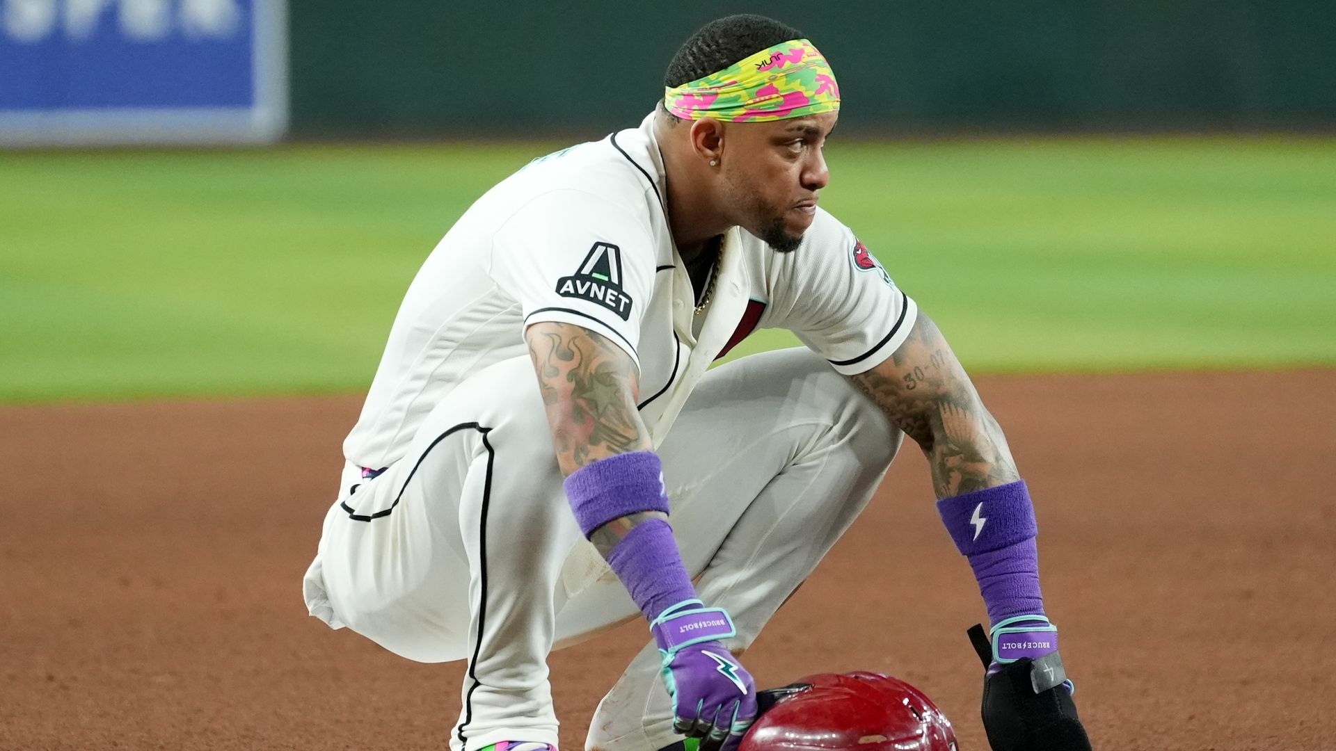 Ketel Marte crouches over a base in a white Diamondbacks jersey, holding a red batting helmet.