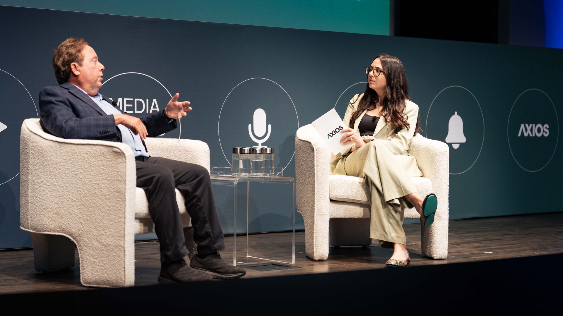IMAX CEO Richard Gelfond speaks with Axios' Kerry Flynn on stage during an event with a blue backdrop.