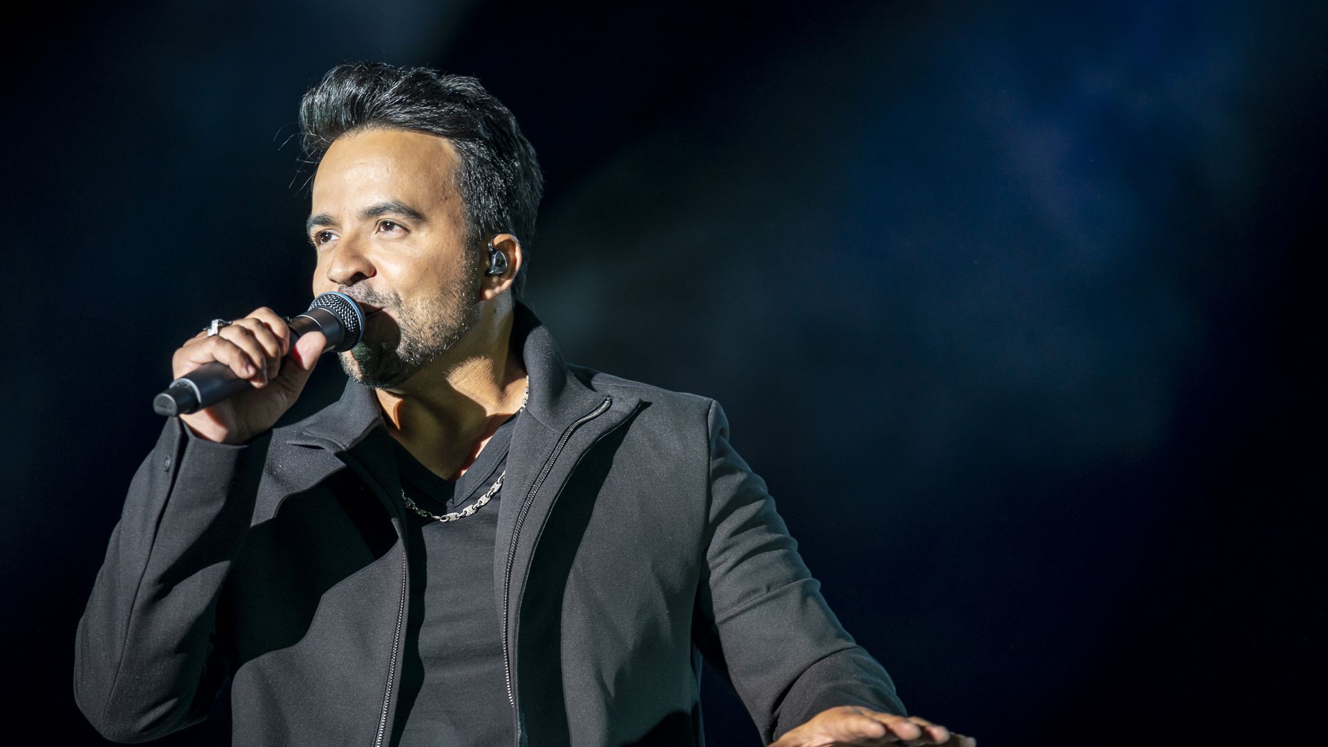 Luis Fonsi sings with a microphone to his mouth with a black background