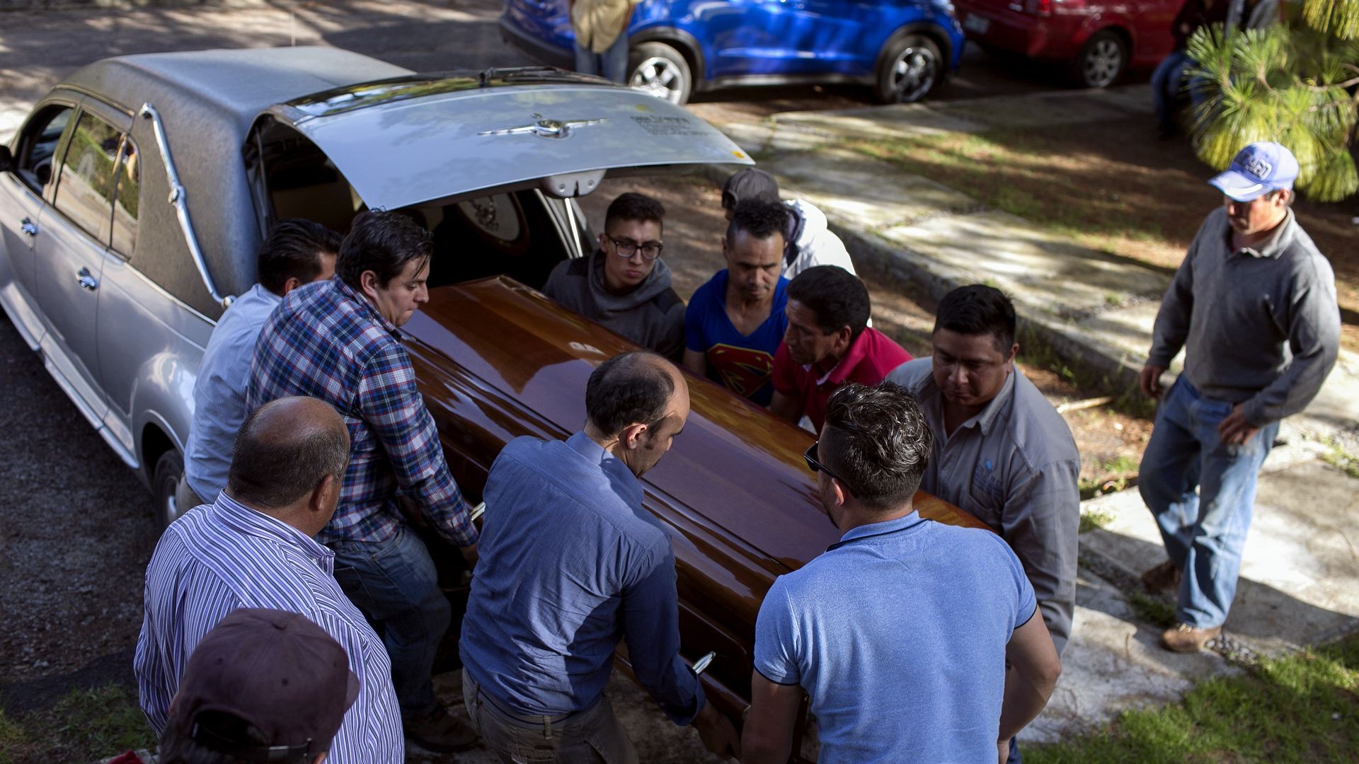 Coffin is pulled out of car trunk by group of people