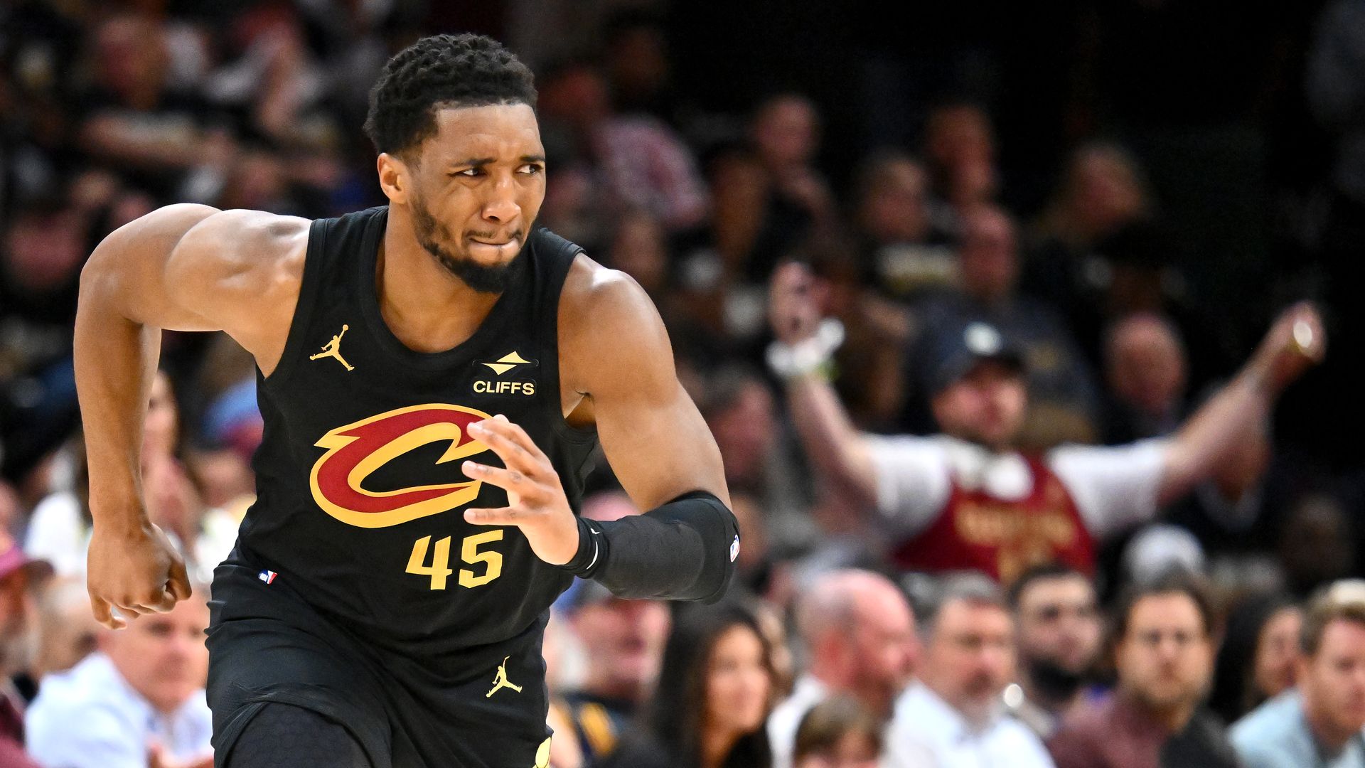 Basketball player in black jersey running up court, grimacing