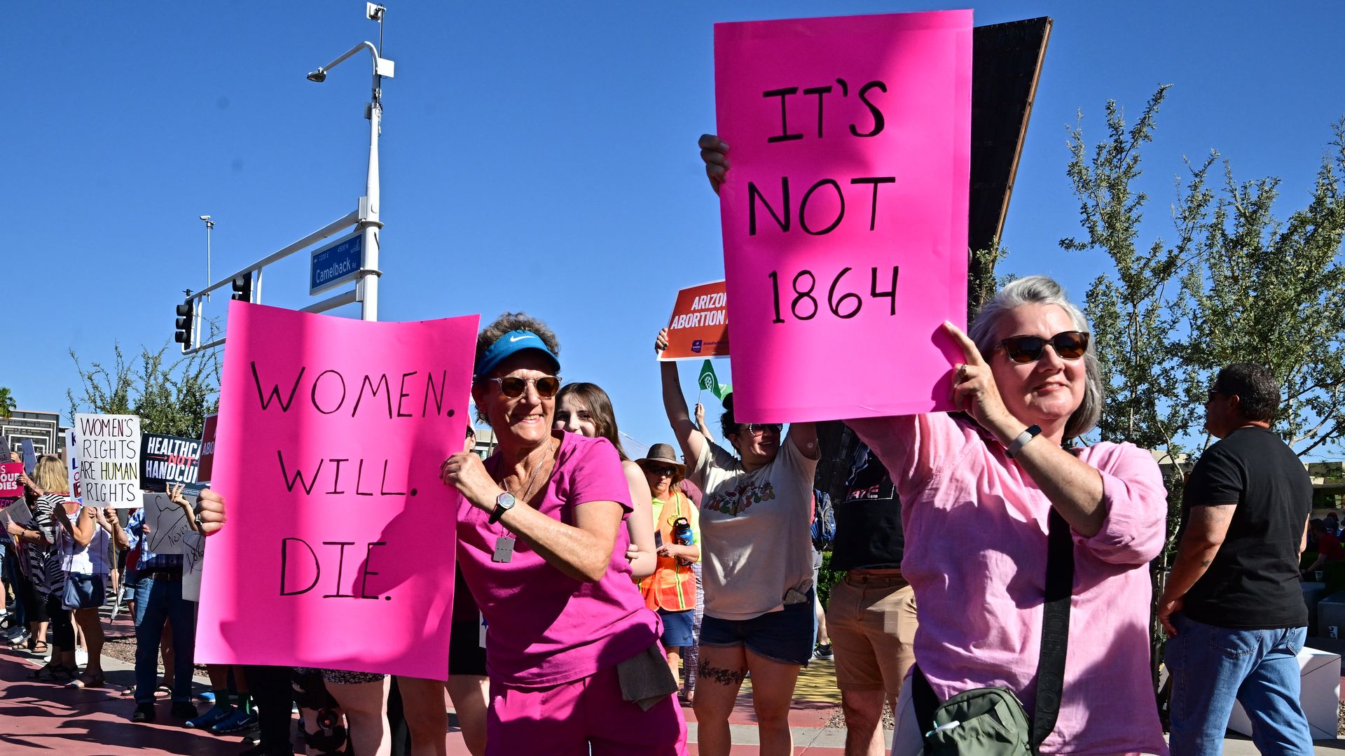 Women holding pink signs that say, "WOMEN WILL DIE" and "IT'S NOT 1864."