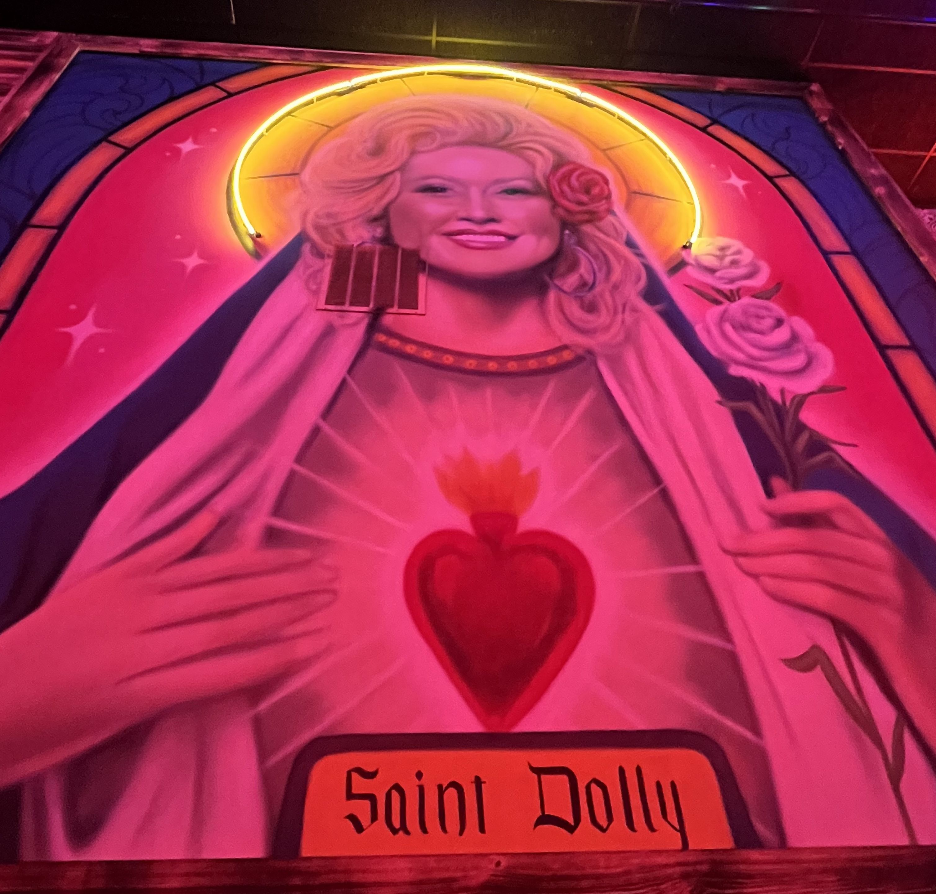 A mural of Dolly Parton that reads "Saint Dolly" and has a halo behind her head. 