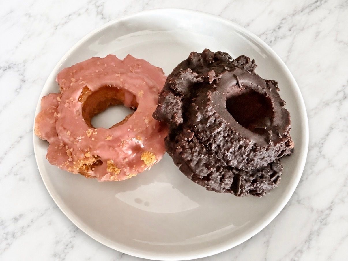 Photo of two donuts, one pink and one brown, sitting on a plate on a table.