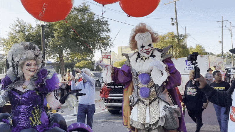A creepy clown walks past with a finger to his lips.