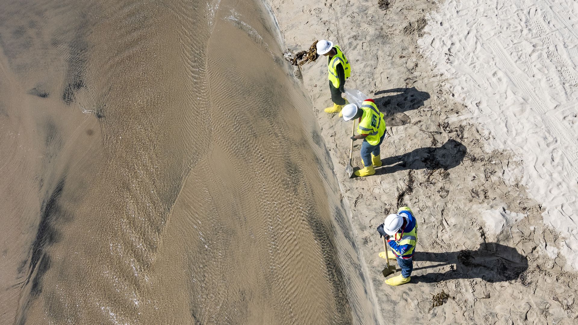 Clean-up crews look for oil washing up near the pier in Huntington Beach, CA on Monday, October 11, 2021 as visitors returned to the beach. 