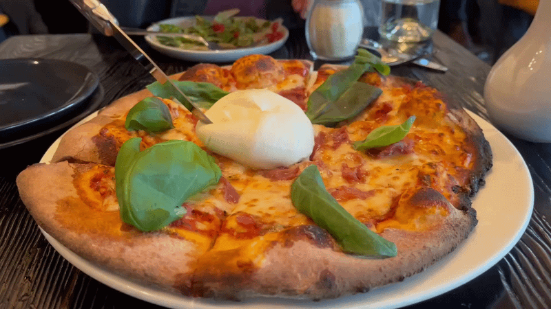 A knife cutting through a burrata ball on a pizza.