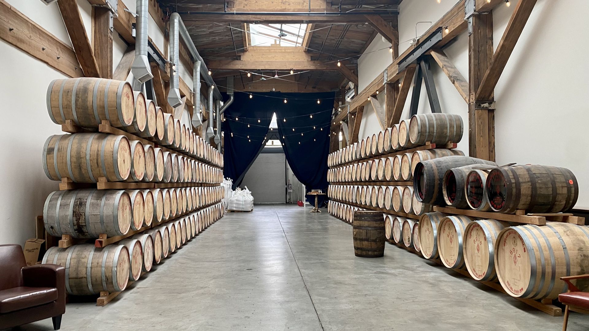 Barrels stacked along the walls in a room with polished concrete floors and skylight windows.