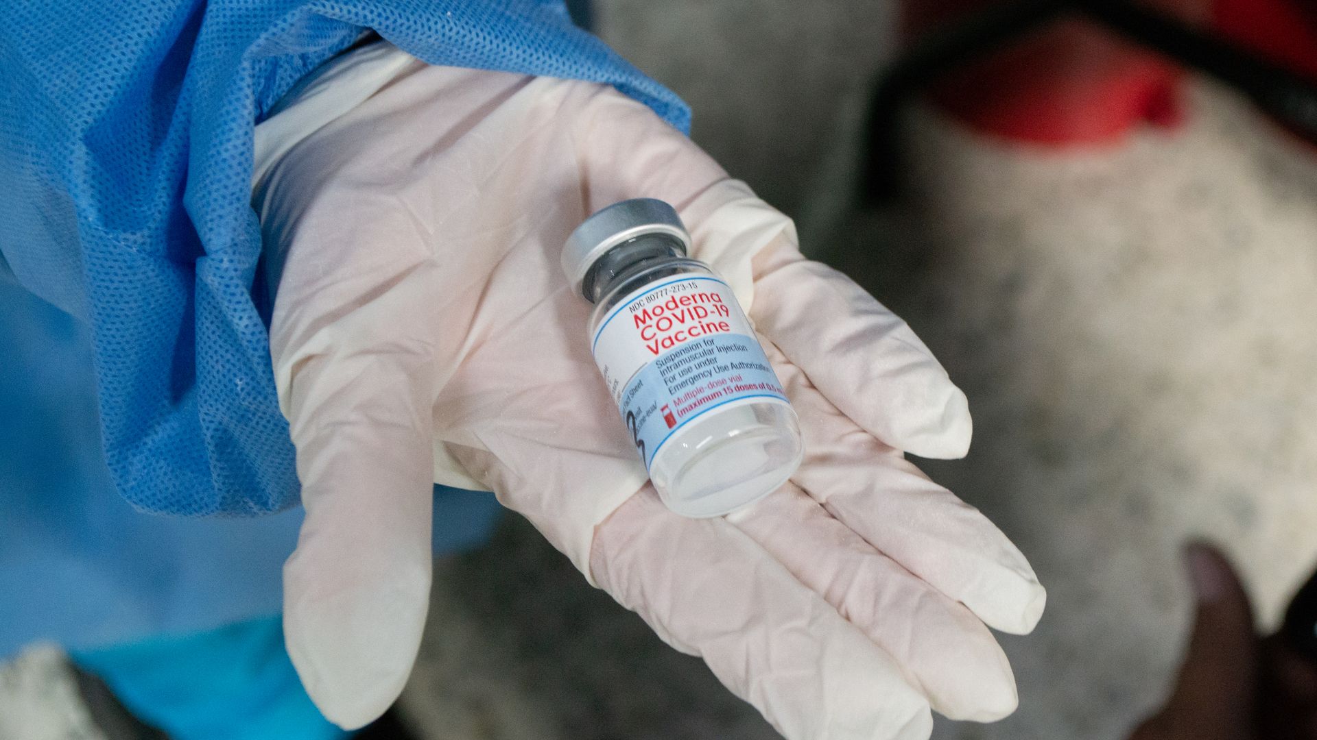 Picture of a hand wearing surgical globes holding a Moderna COVID-19 vaccine vial