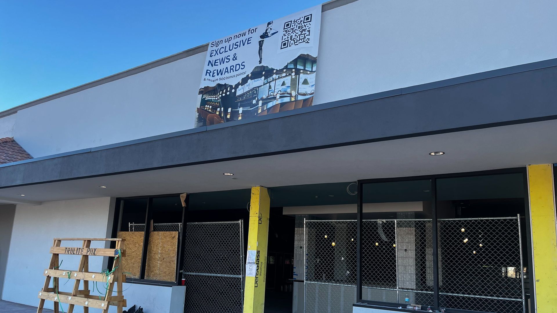 A store front with a boarded up window and a banner above the doors. 