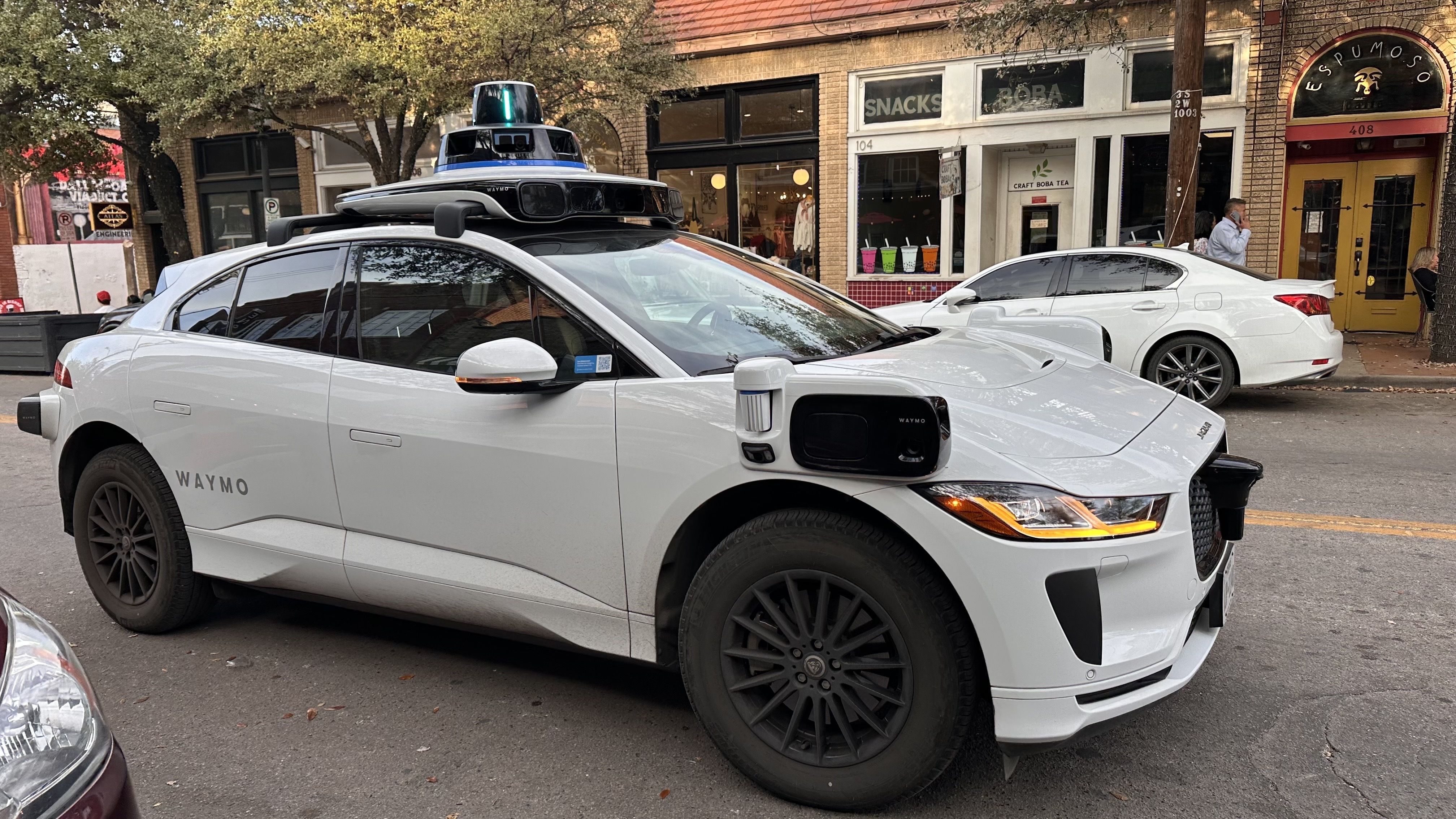 White Waymo autonomous car equipped with multiple sensors and cameras, parked in Bishop Arts.