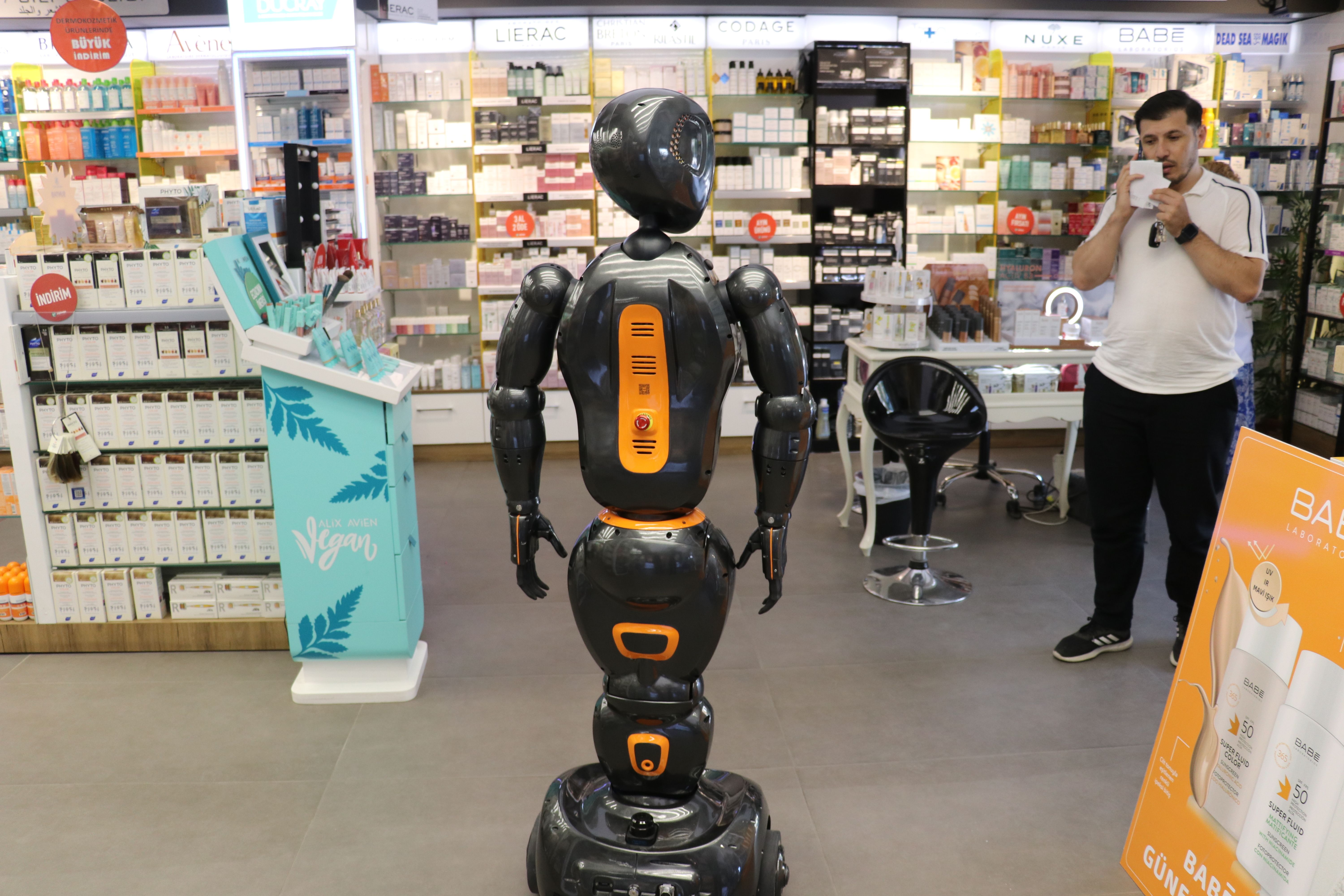 A humanoid robot stands in a pharmacy, surrounded by shelves of pill bottles.