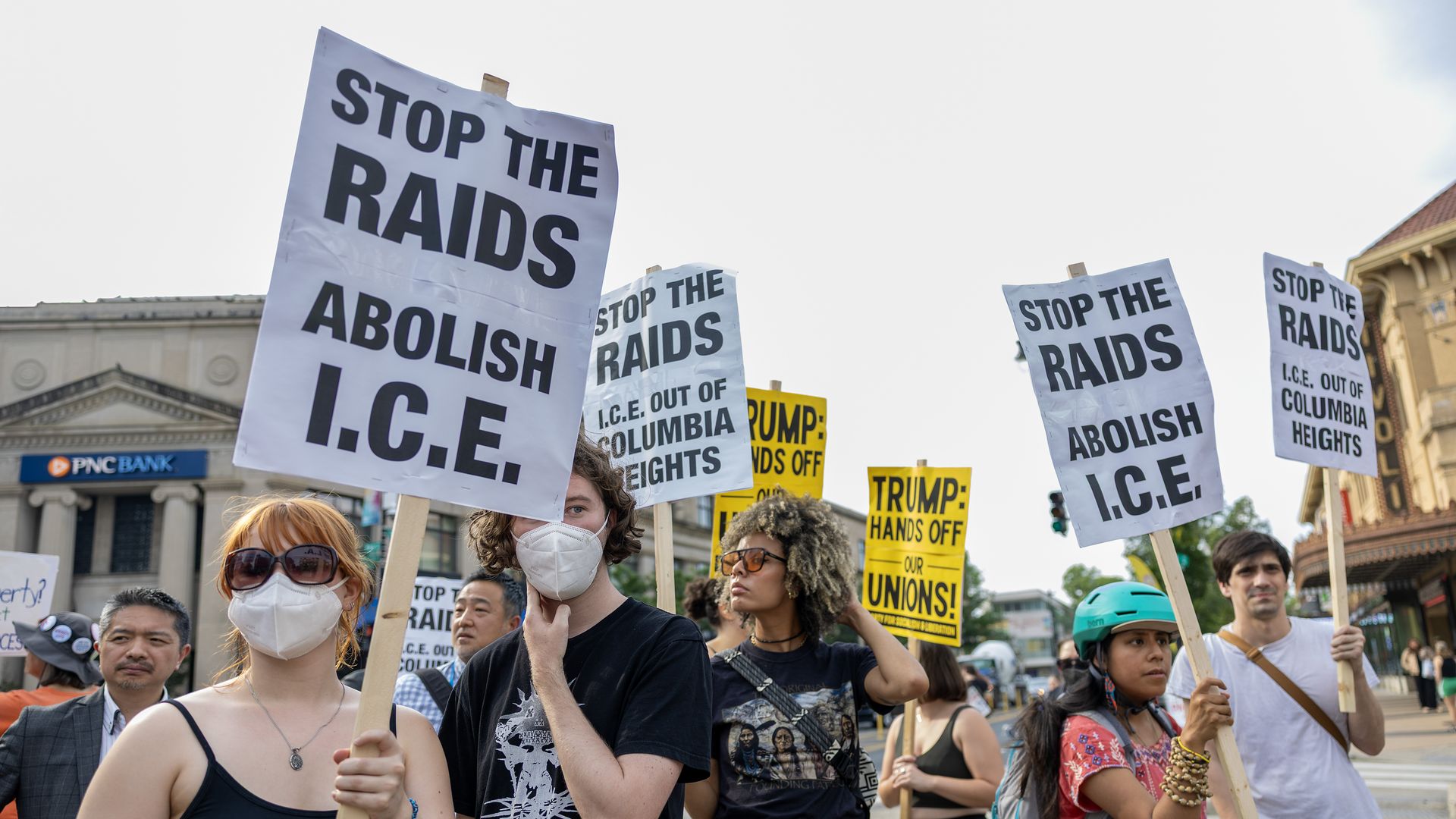 Protesters, some of whom are wearing masks, hold anti-ICE signs at a protest in Washington, DC.