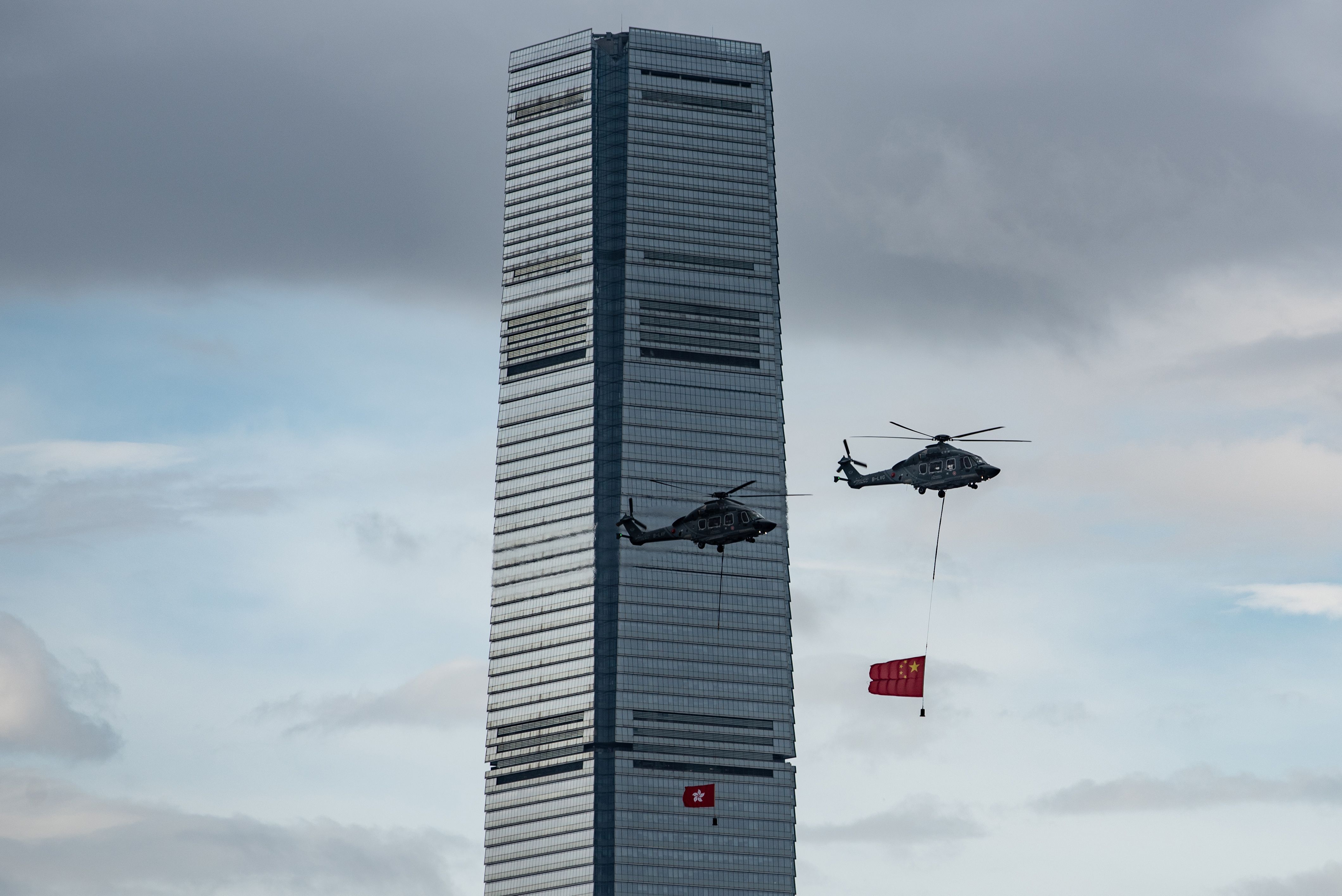 elicopters fly across Victoria Harbour carrying a Hong Kong (L) and China (R) flag during the annual flag raising ceremony to mark the 22nd anniversary of the city's handover from Britain to China.