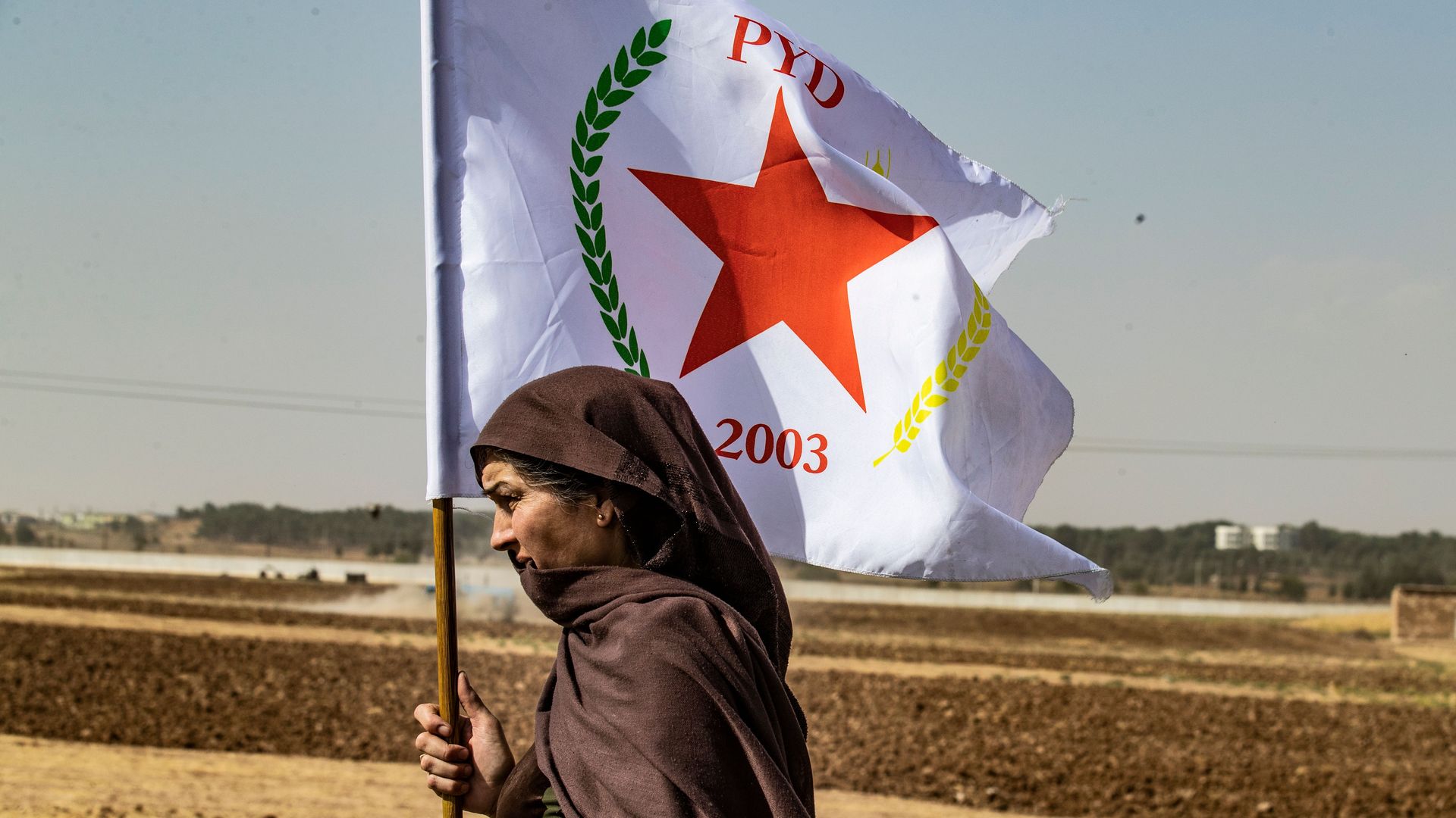 A Syrian Kurdish woman waves the flag of the Democratic Union Party during a demonstration against Turkish threats in Syria near the Turkish border.