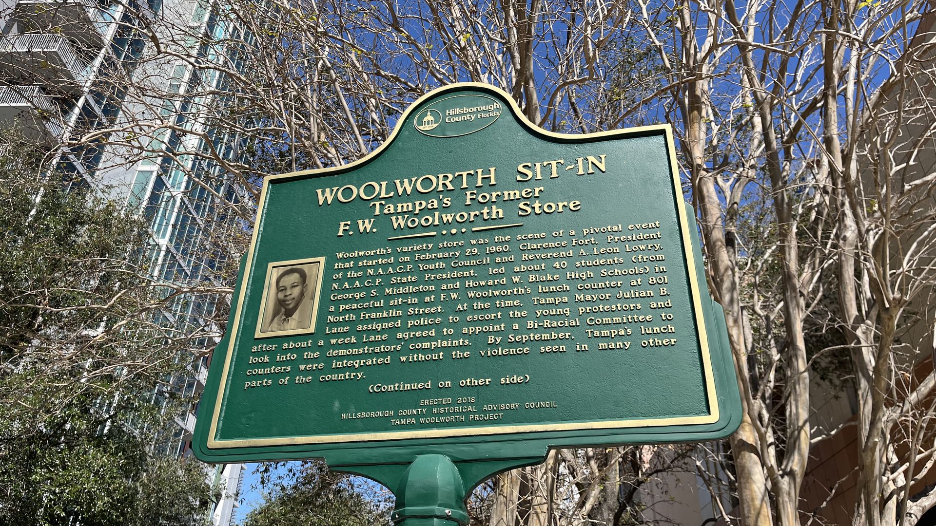 A green historic marker with gold text that reads "WOOLWORTH SIT-IN Tampa's former F.W. Woolworth Store."