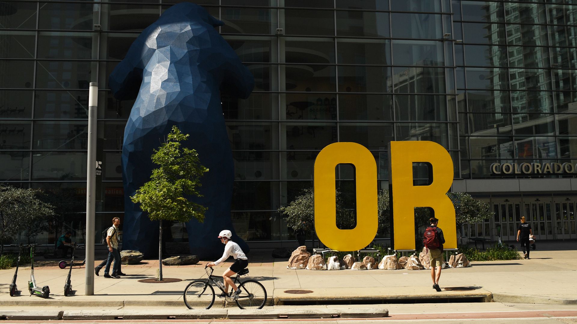 Pedestrians and a bike rider make their way to the glass-clad Colorado Convention Center.