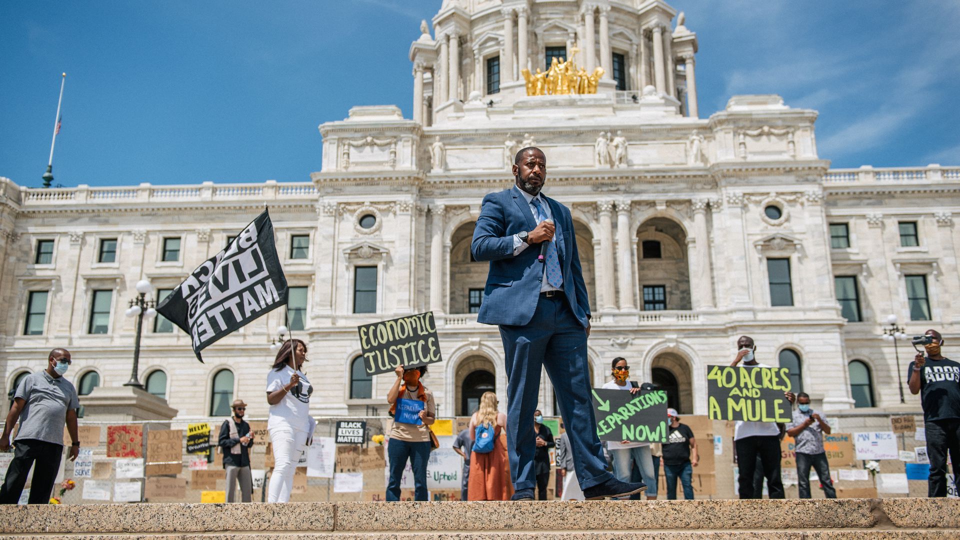 State Rep. John Thompson (DFL-St. Paul) stands in front of protesters waving signs at the Minnesota State Capitol.