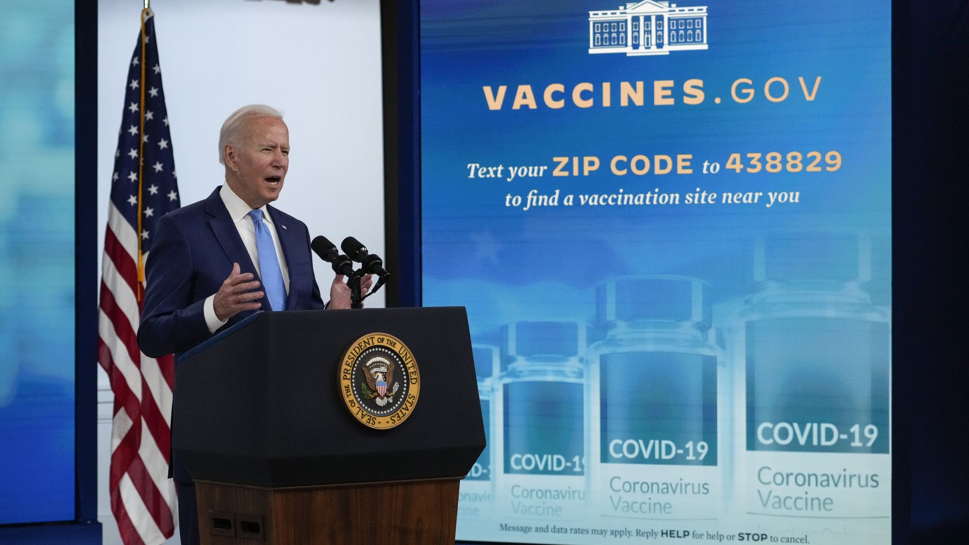 Photo of Joe Biden speaking from behind a podium with a screen next to him that says "text your zip code to find a vaccine site"