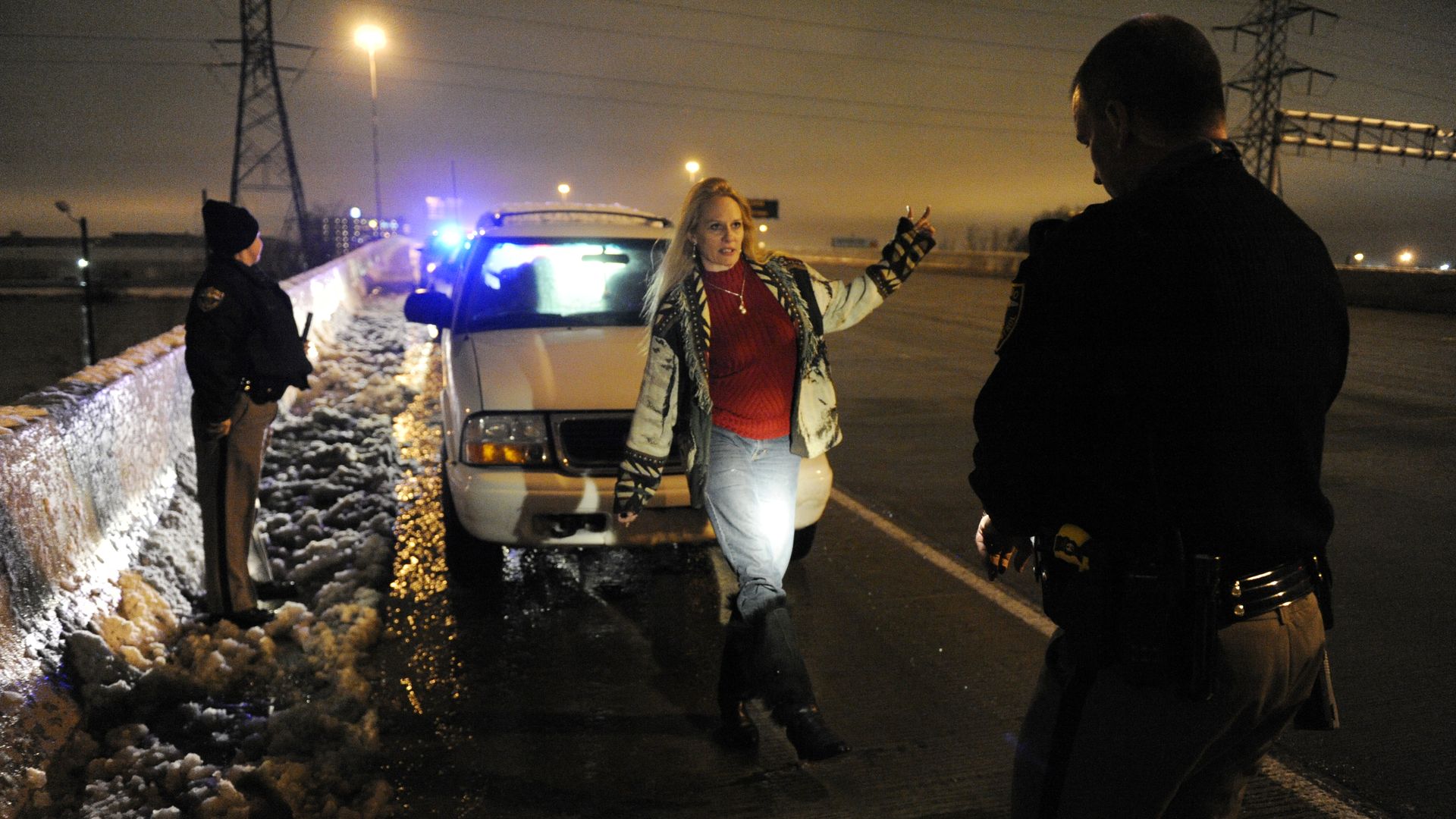Woman performs sobriety test in front of a copy in the dark on the side of a highway