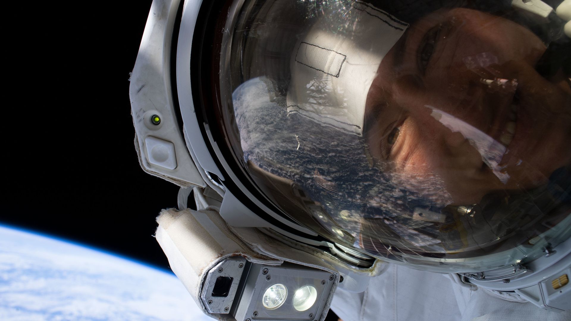 A NASA astronaut looks into a camera during a spacewalk with Earth in the background