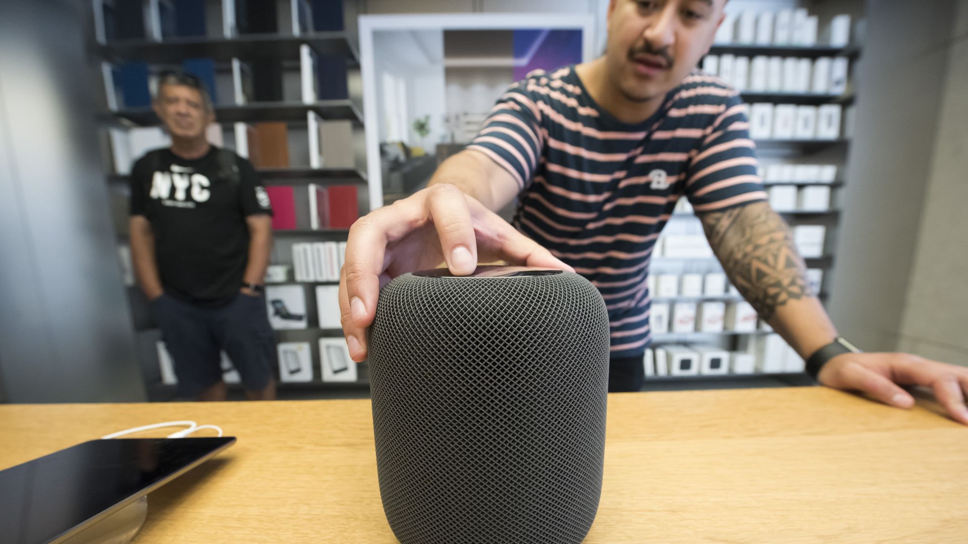 Apple HomePod smart speaker on a table while a man is palming it. 