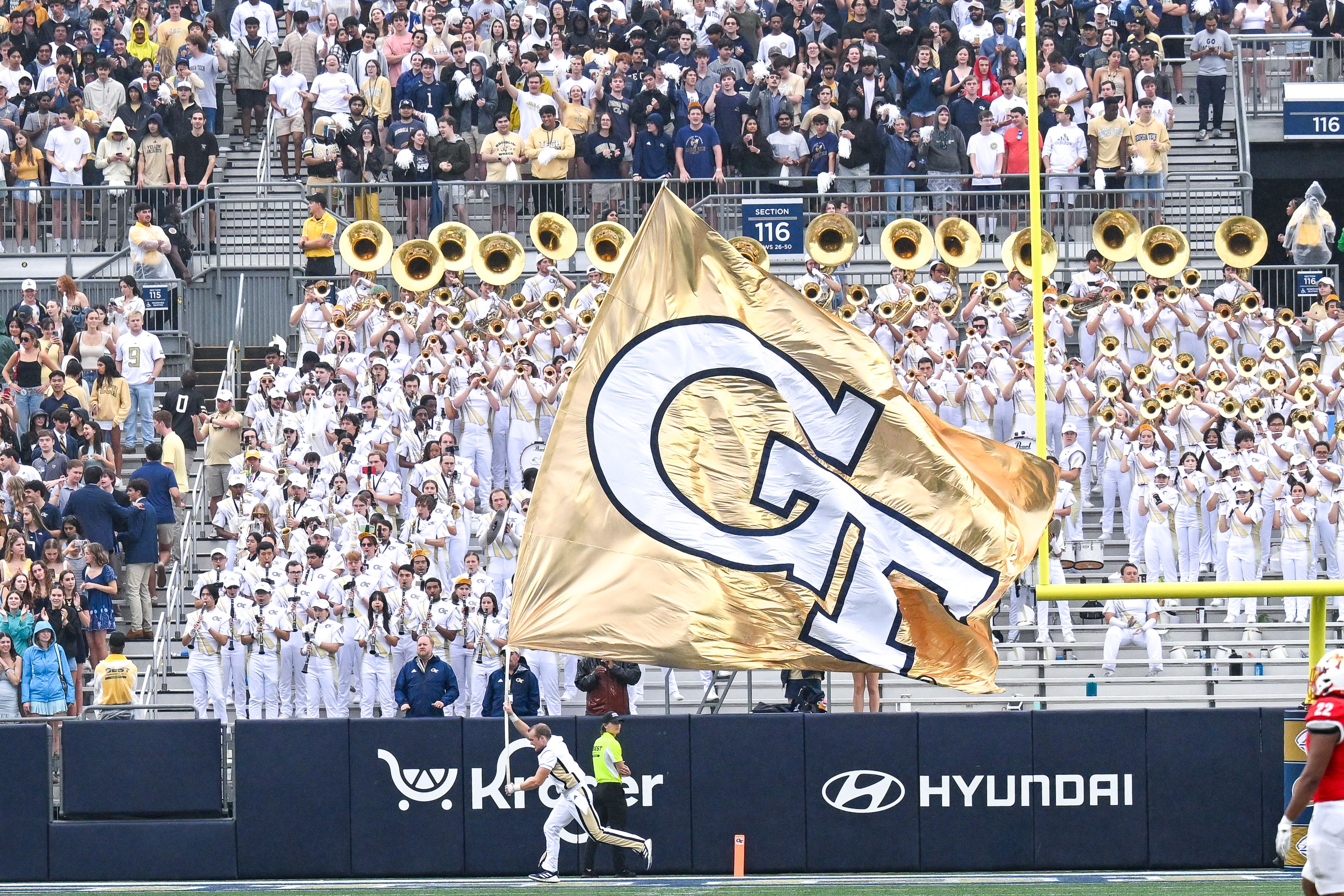 A yellow flag with the letters GT being ran across a field by a cheerleader