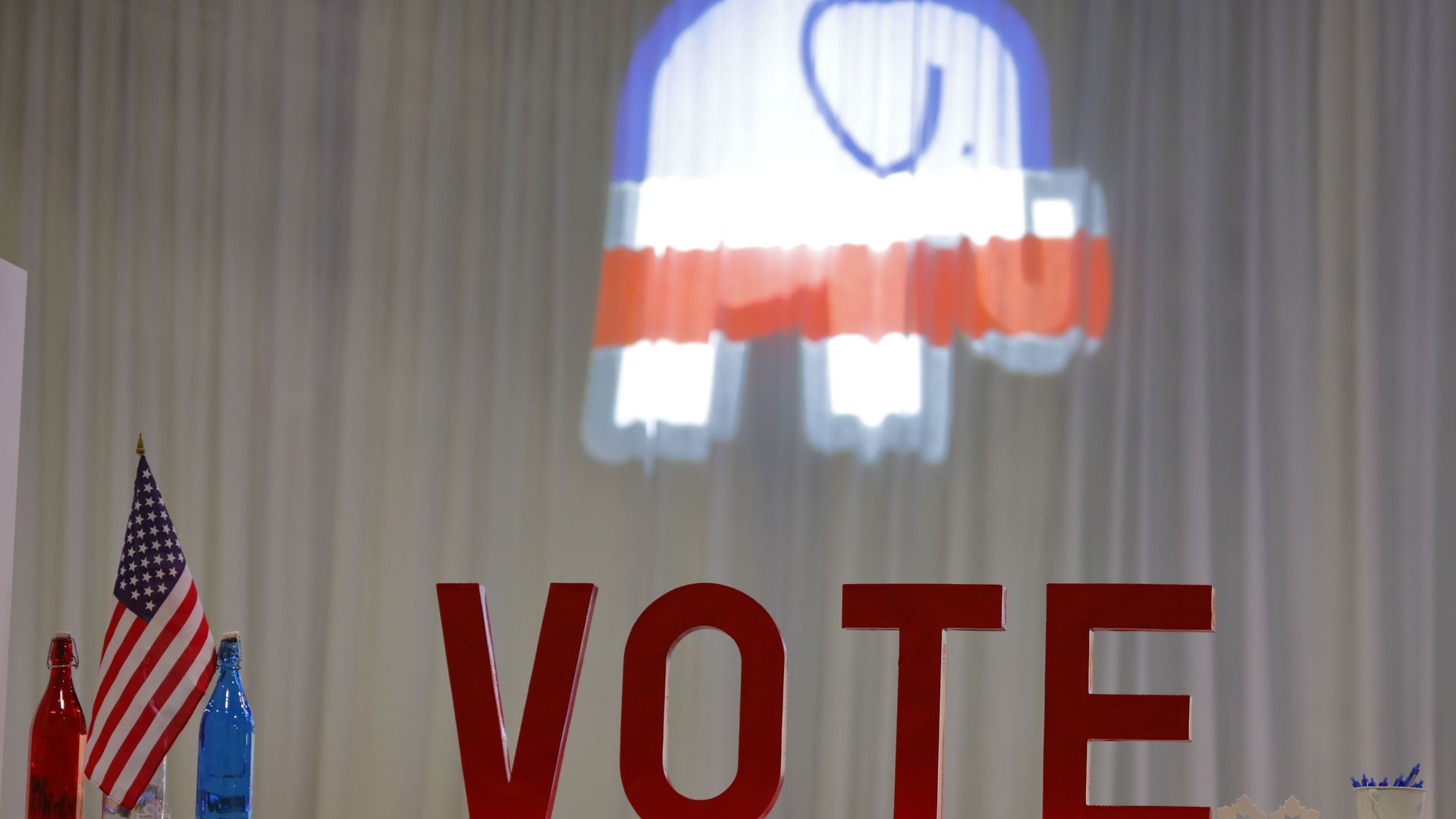 A Republicans elephant is lit up on a curtain behind a table that says VOTE