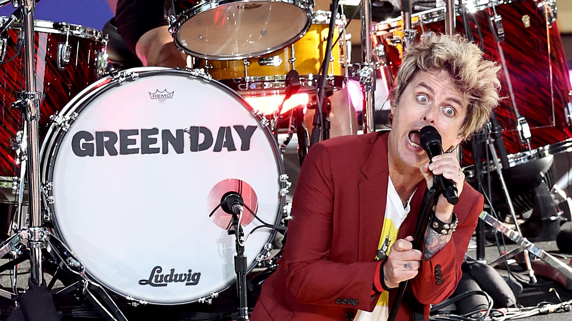 A musician sings on state in front of a drum that says "Green Day".