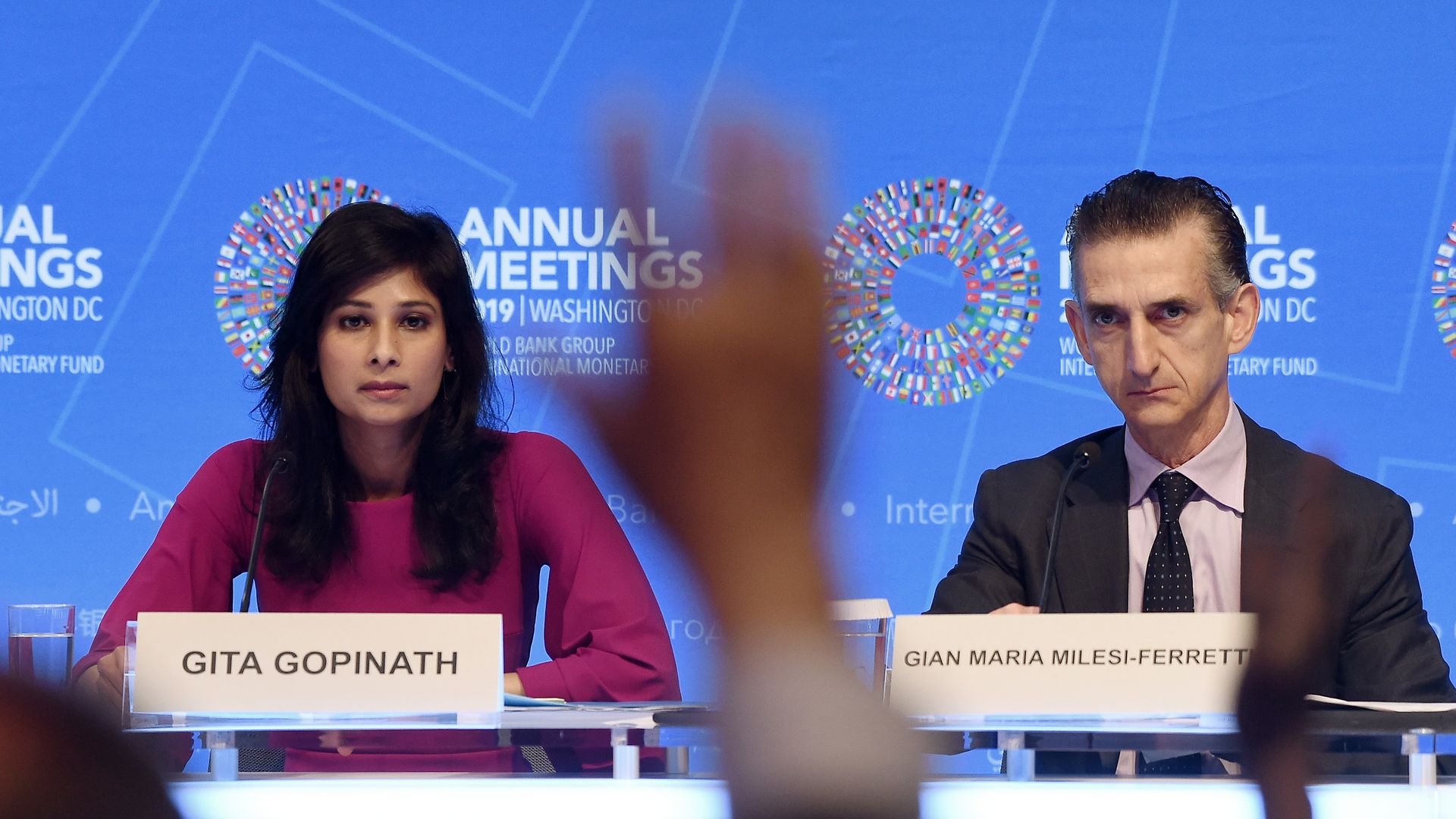 The IMF chief economist sits behind a dais and a hand is raised in front of her.