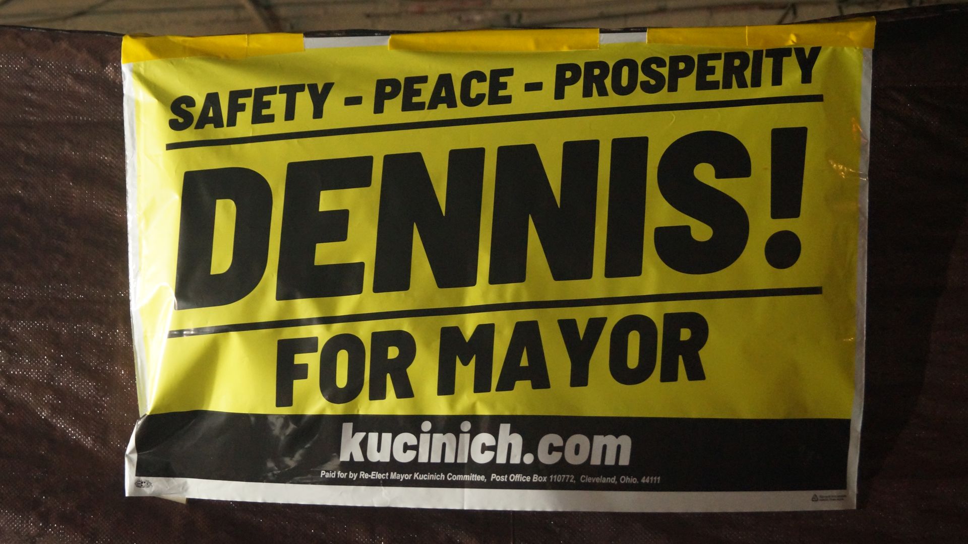 A campaign yard sign for Dennis Kucinich, with Dennis! in black letters on a yellow background