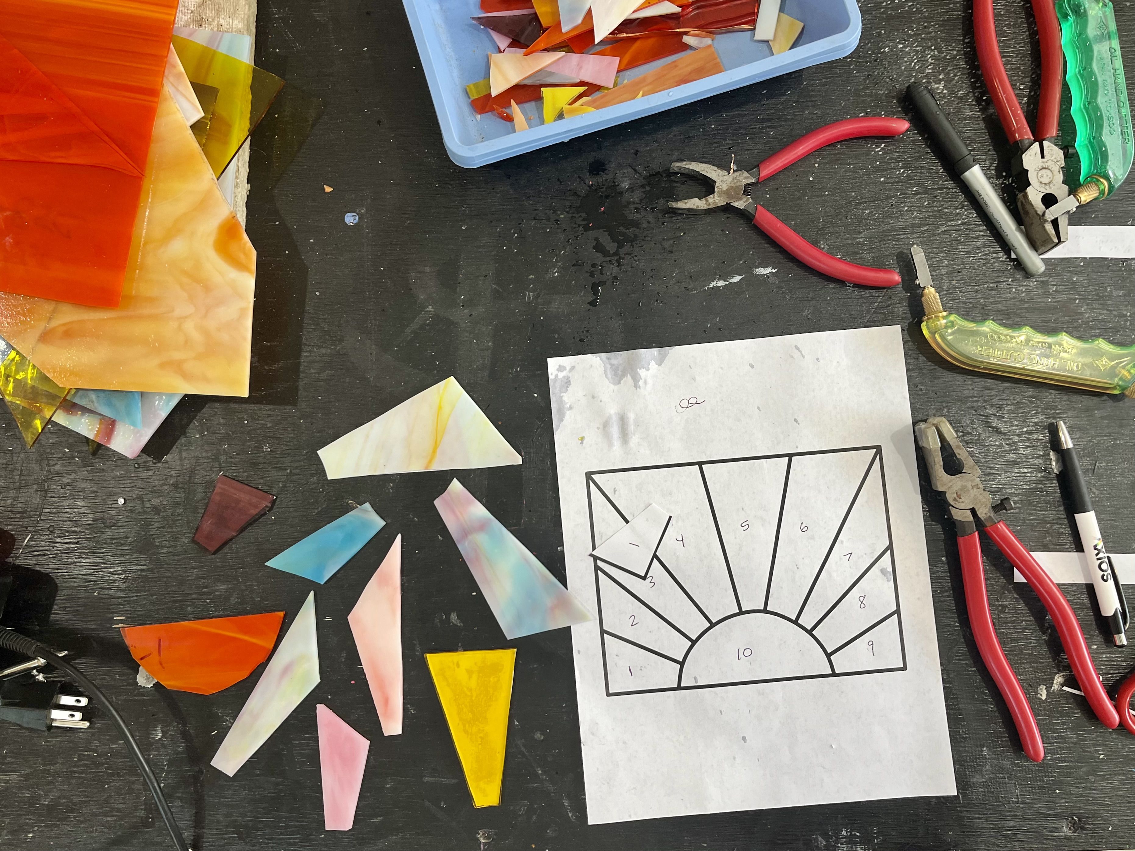 An overhead view of a table with a numbered design and pieces of glass cut in shapes to match the design.