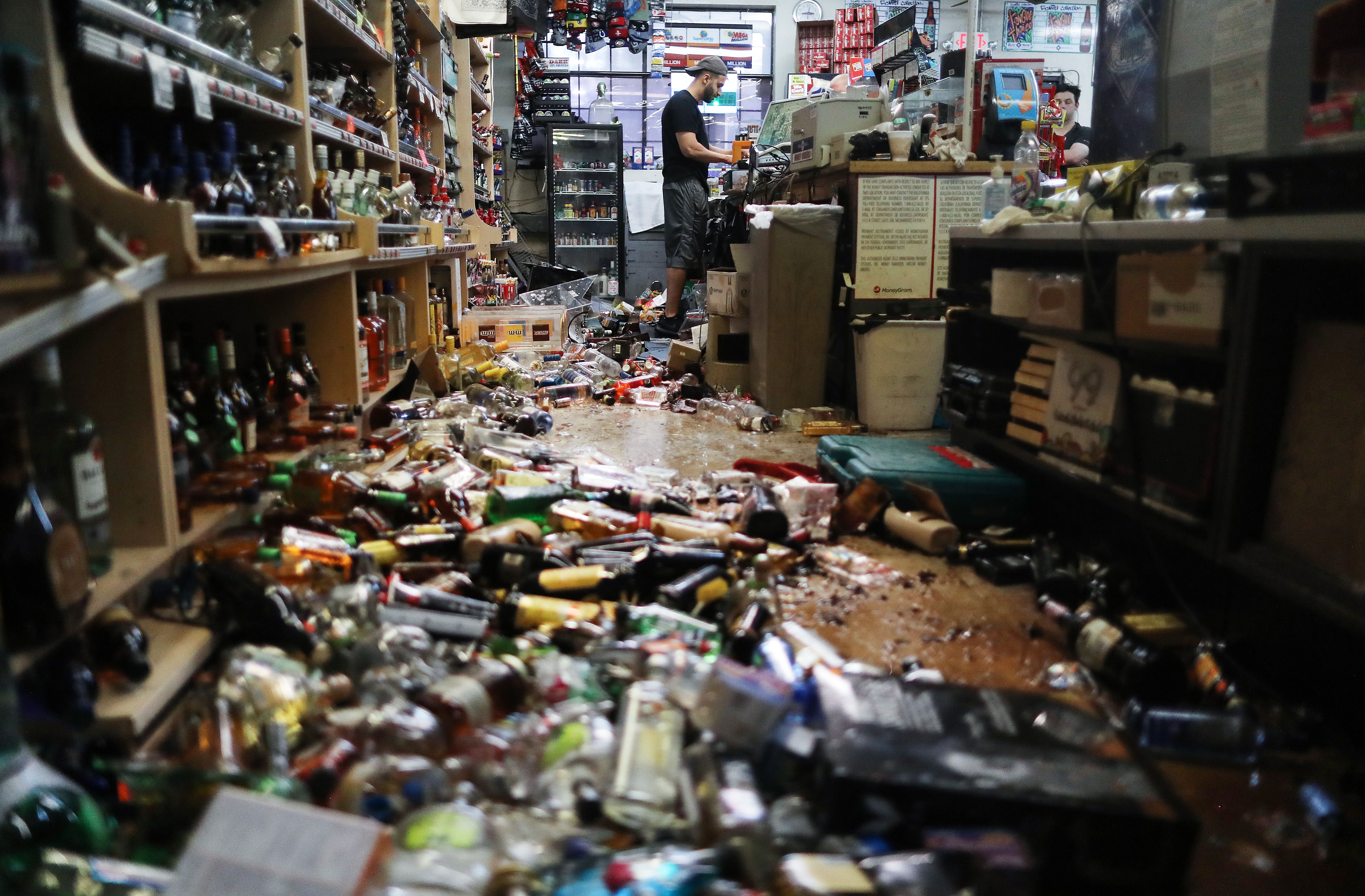 This image shows a liquor store aisle swamped with broken bottles and spilled alcohol. 