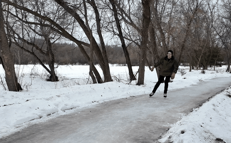 A man in a green jacket ice skating quickly through a path of ice in the forest.
