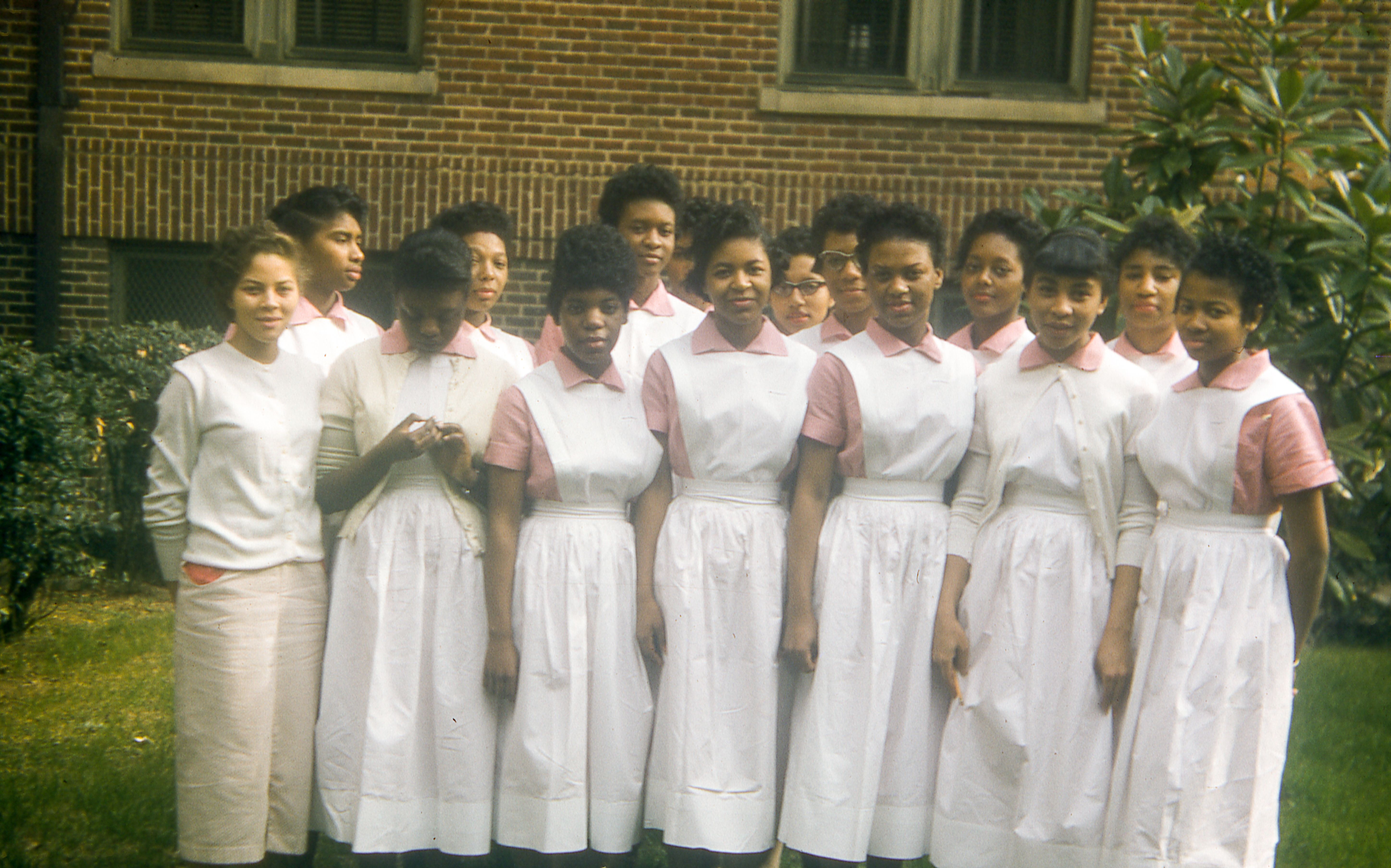 Graduating class of nurses at the Grady Memorial Hospital in Atlanta, Georgia, stand and pose for a group photo wearing white nurse gowns with pink undershirts on a lawn in front of the brick building of the hospital, June, 1957. (Photo via Smith Collection/Gado/Getty Images).