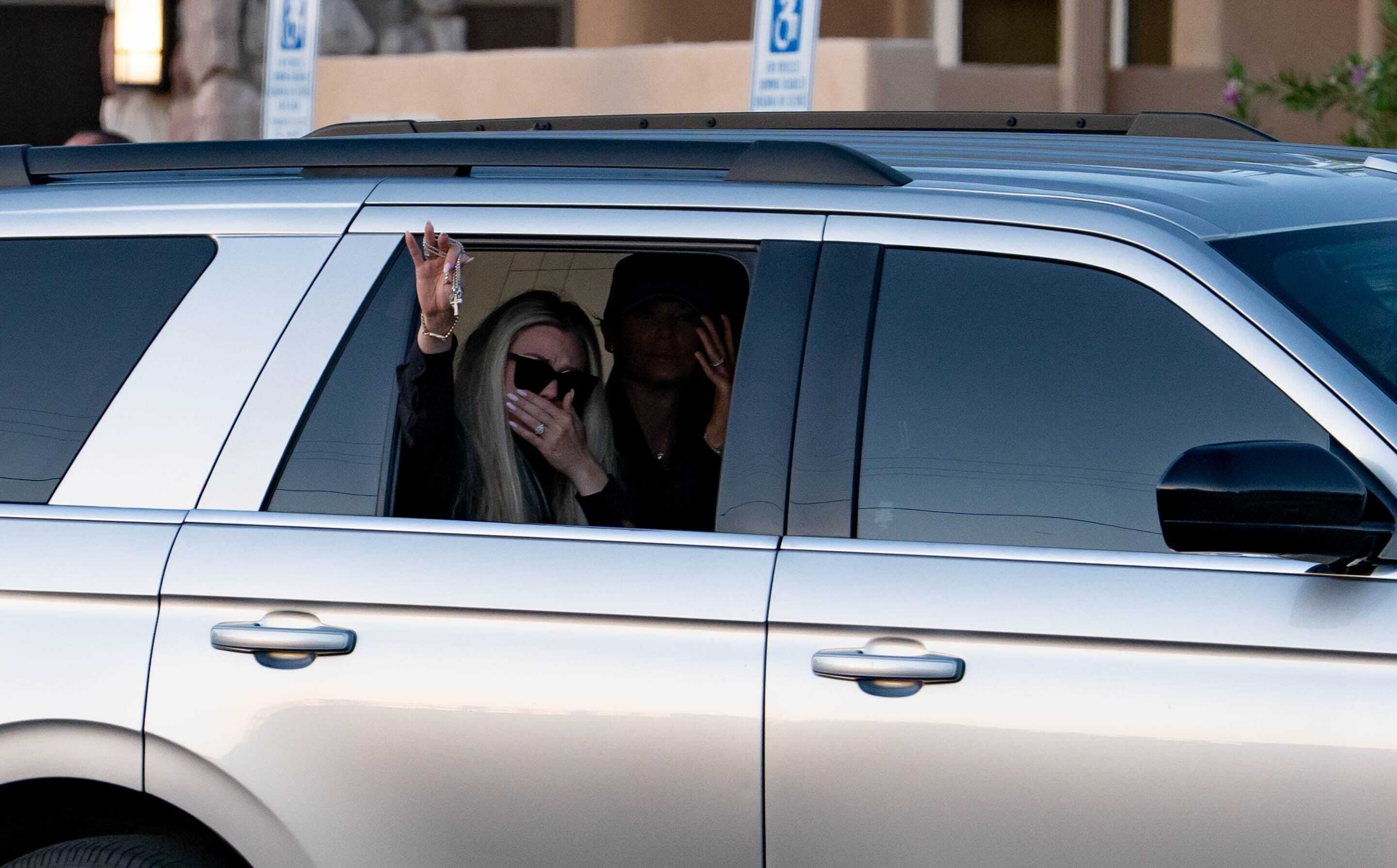 Erika Kirk waves from the inside of a silver car