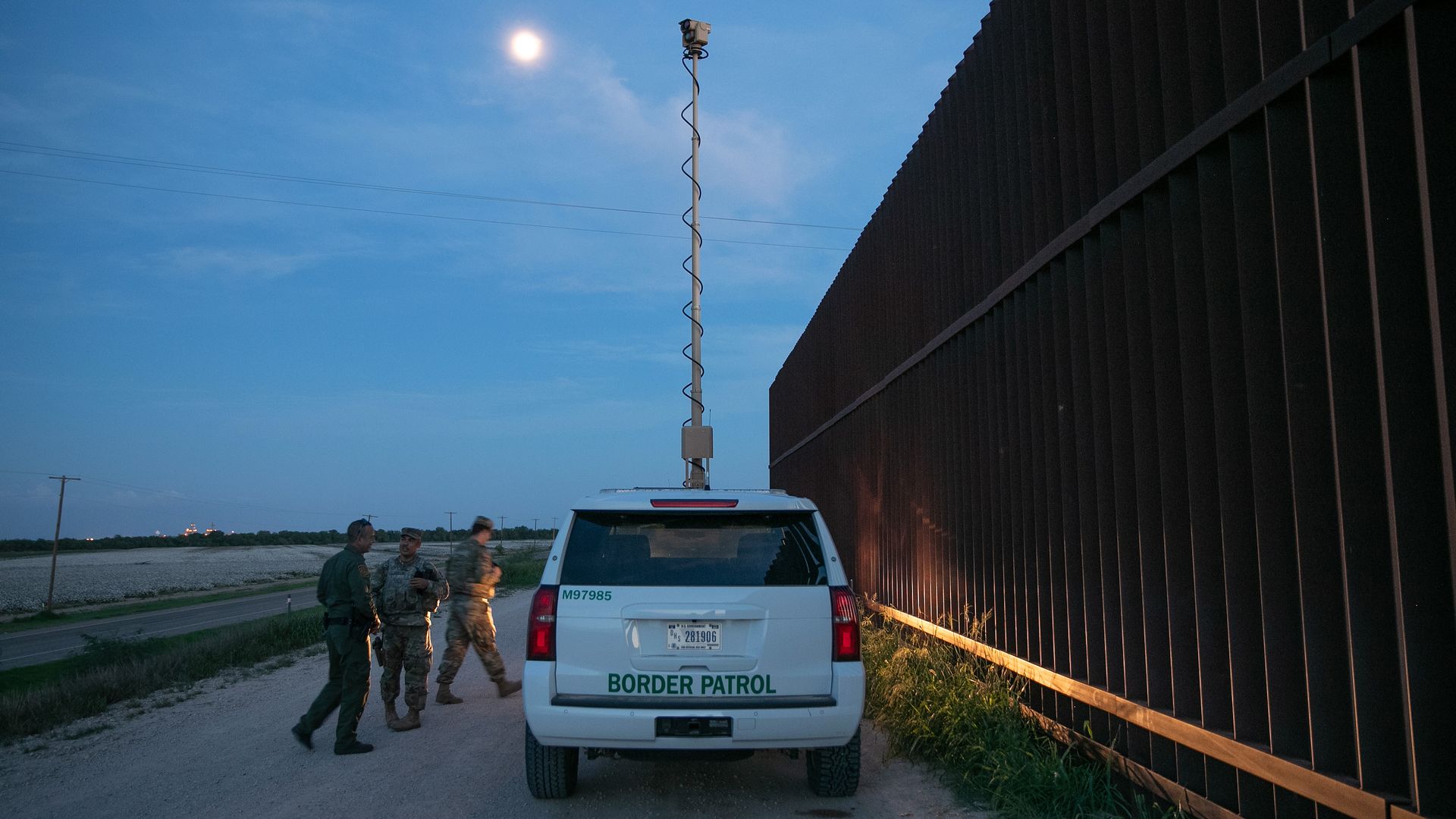 Border patrol car parked by a border fence at dusk. 