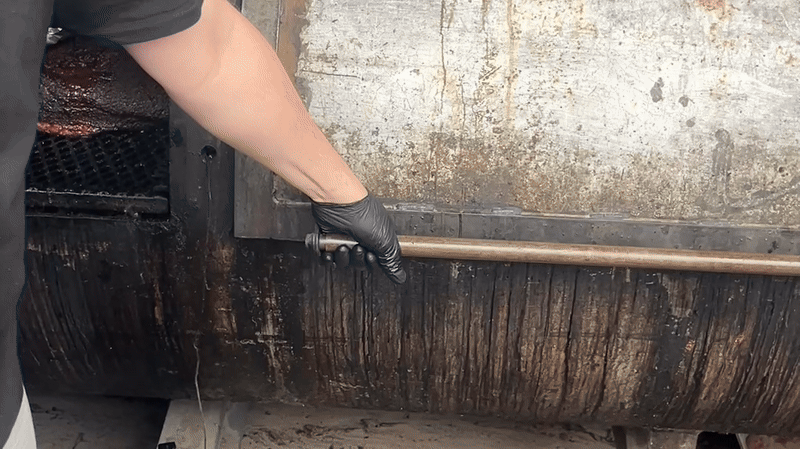 Video of a hand opening a big smoker showing a bunch of meat inside.